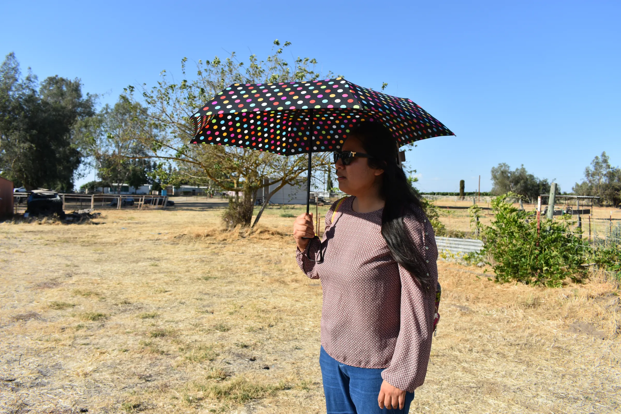 Juanita Pérez Sierra shades her face from the blistering sun on Comunidad Nuevo Lago’s “ranch,” seven acres of communal land residents use for big events like a recent quinciñera, in Fresno, California, U.S., July 1, 2025. Thomson Reuters Foundation/Rachel Parsons