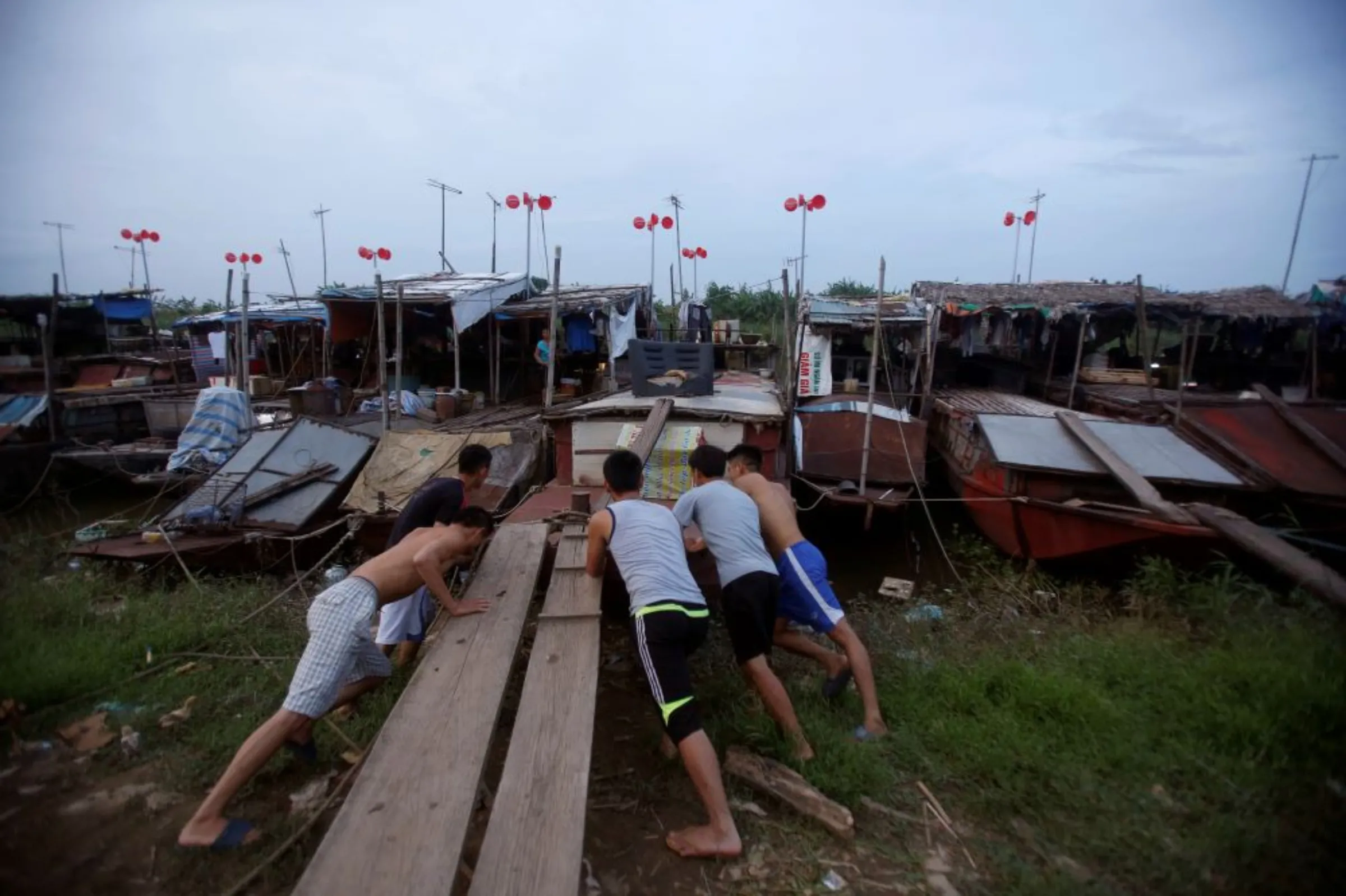 Men move a boat in front of a wind power system made from plastic buckets at a floating village in Hanoi, Vietnam July 1, 2016