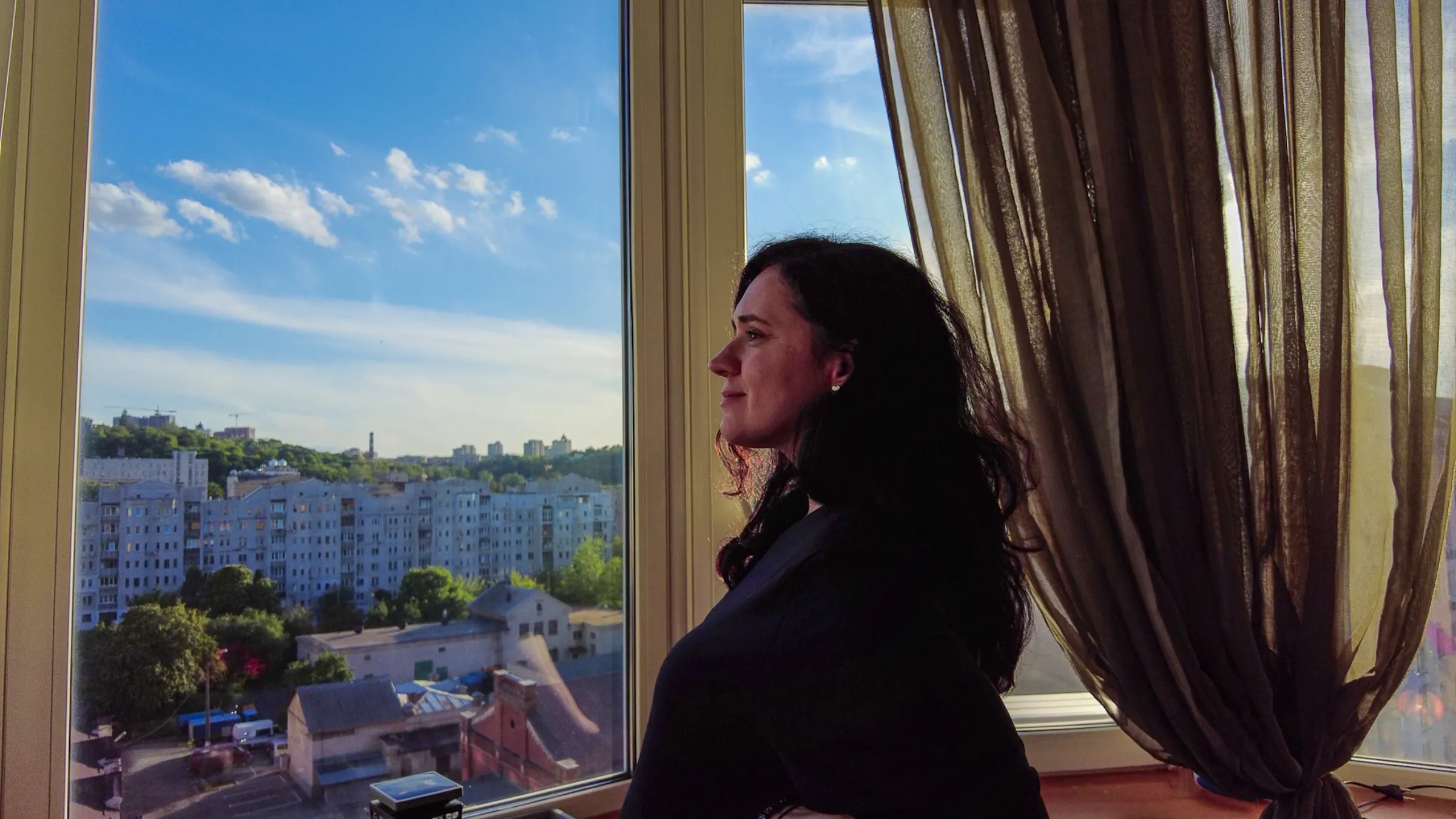 Olena Rozvadovska, who is pregnant, looks out the window of her apartment in Kyiv where she regularly watches strikes and drone attacks. Kyiv, Ukraine, May 23, 2025. Thomson Reuters Foundation/Danielle Robertson