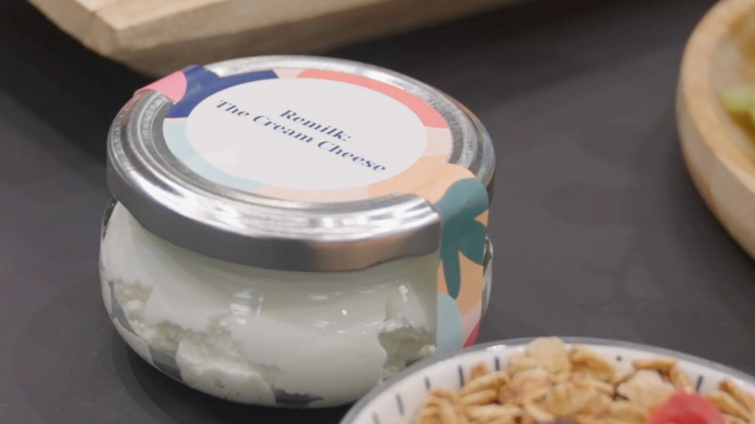 A still from the Context video 'Can lab-grown milk solve dairy’s climate problem?' showing a jar of cream cheese on a table next to items of food