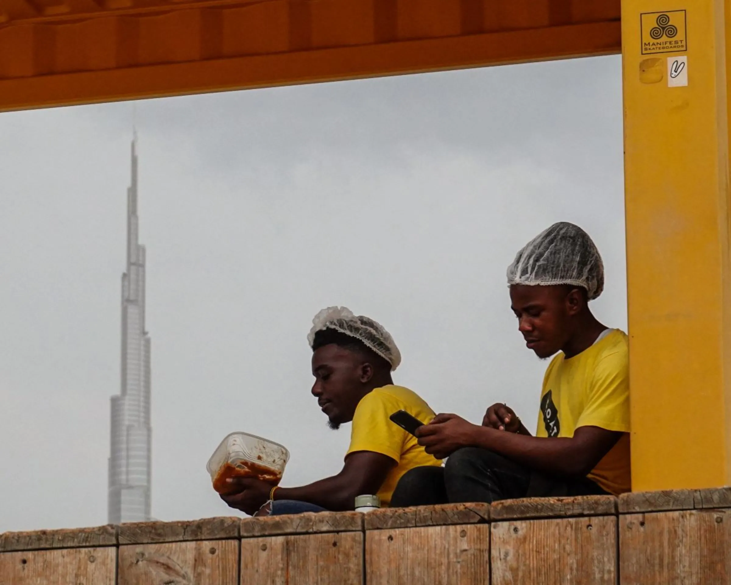 Two workers have a meal while resting with the Burj Khalifa tower seen in the background in Dubai, United Arab Emirates, July 26, 2022