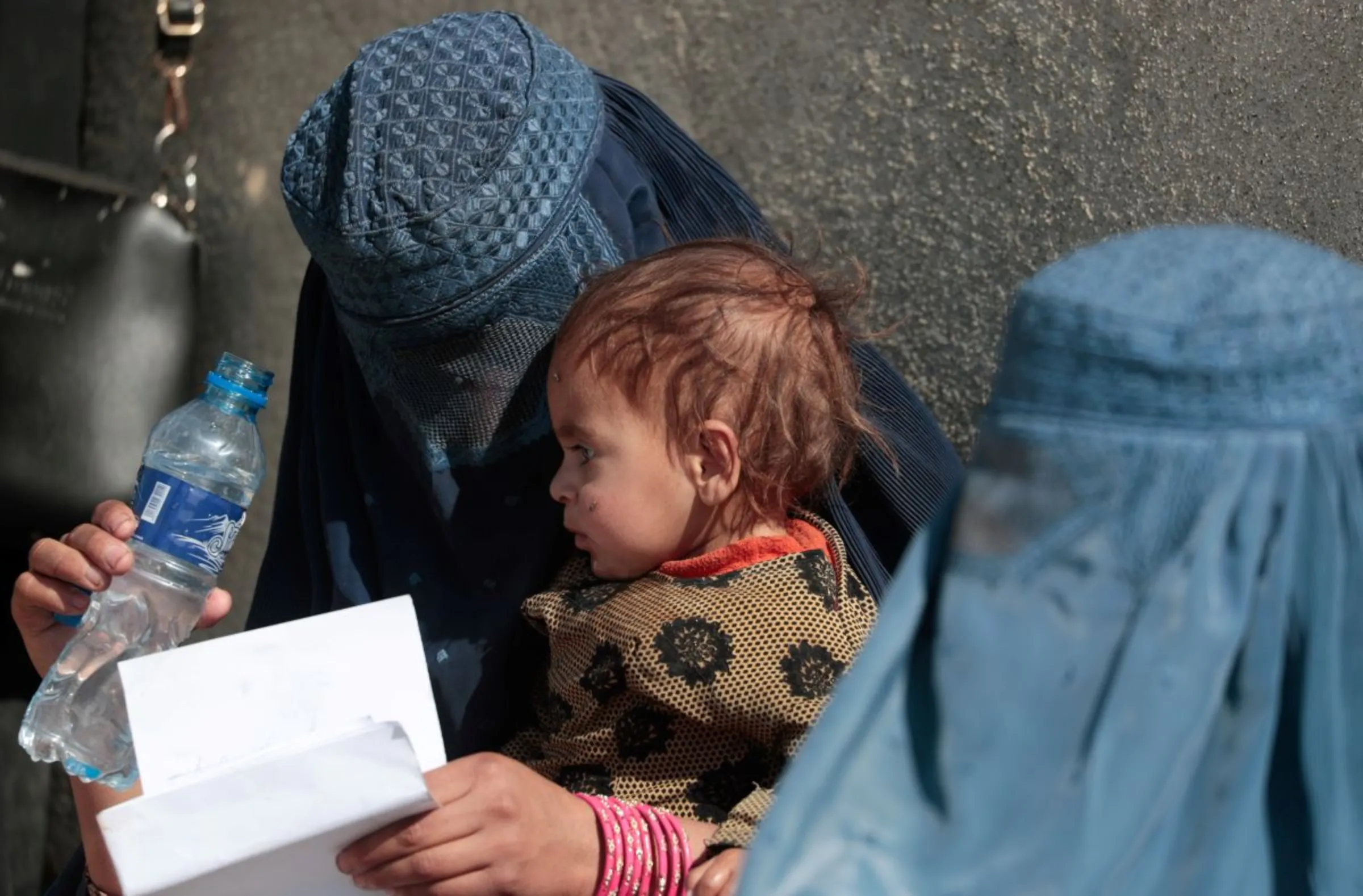 A displaced Afghan woman holds her child as she waits with other women to receive aid supply outside an UNCHR distribution center on the outskirts of Kabul, Afghanistan October 28, 2021