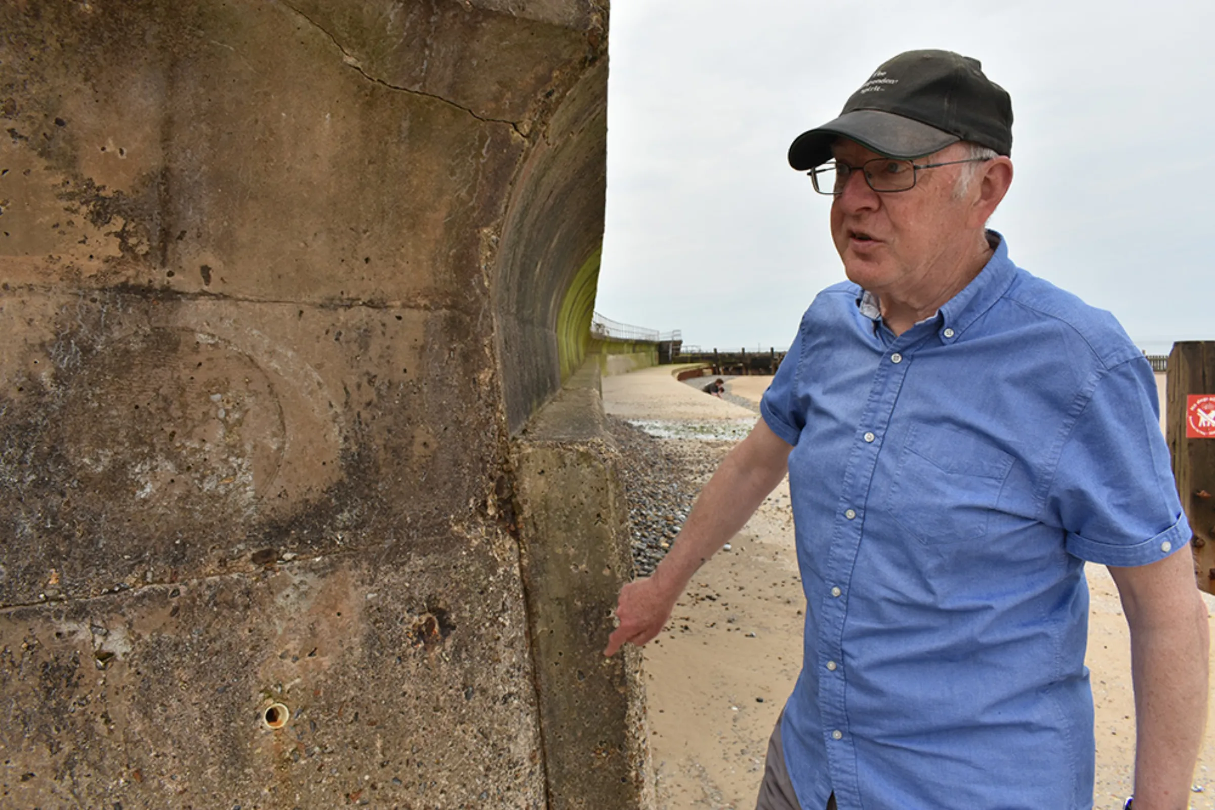 Longtime Overstrand resident Gordon Partridge points out repairs and reinforcement to the old sea wall made over the years in the small Norfolk village in England, June 17, 2023. Thomson Reuters Foundation/Rachel Parsons