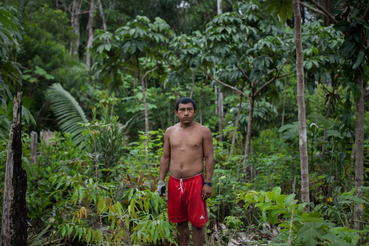 A man stands wearing red shorts surrounded by the rainforest