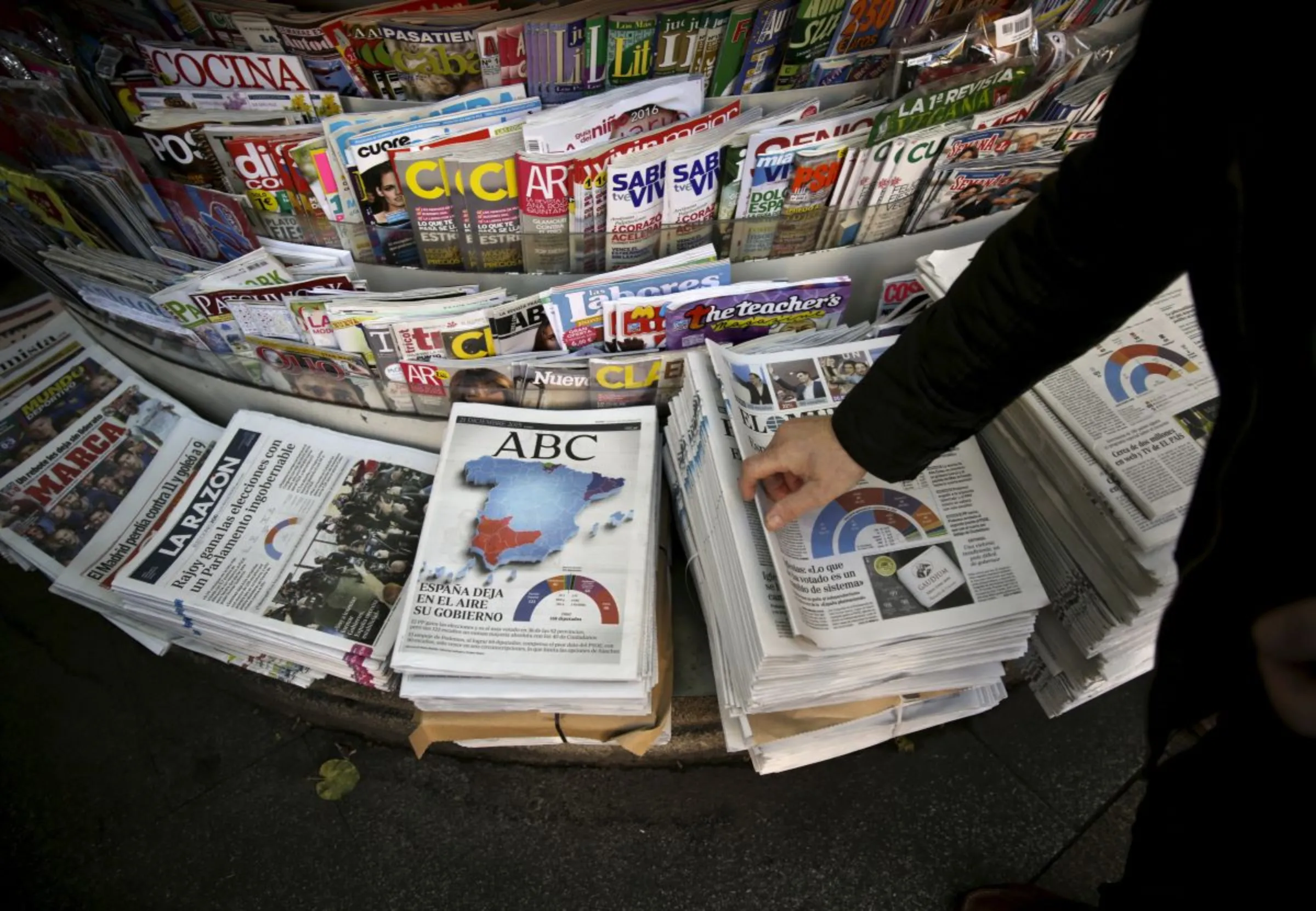 A man takes a newspaper at a kiosk in central Madrid, Spain, December 21, 2015