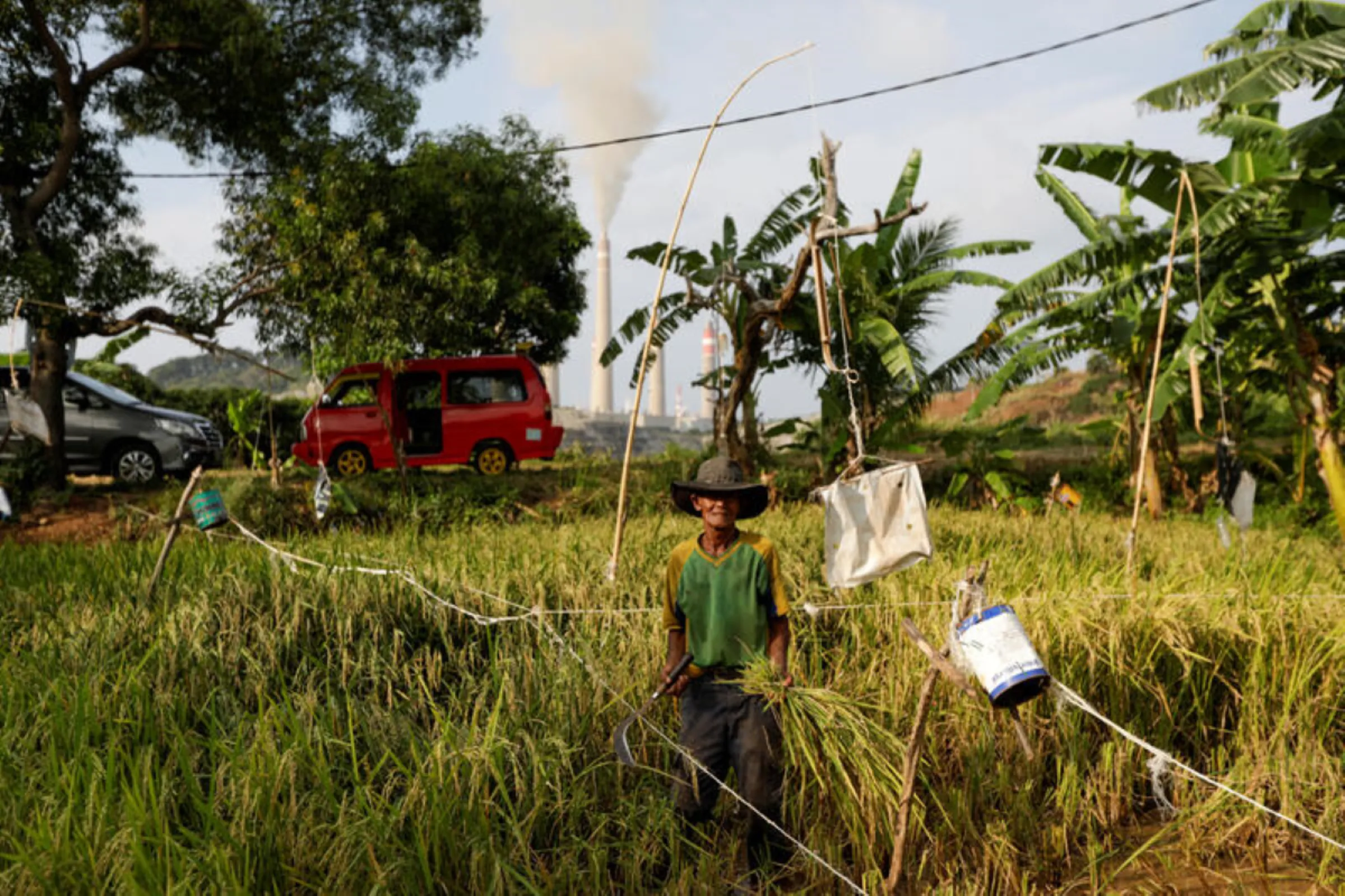 A local farmer looks on as he works on a paddy field at a village near a coal-fired power plant owned by Indonesia Power in Suralaya, Banten province, Indonesia, July 11, 2020