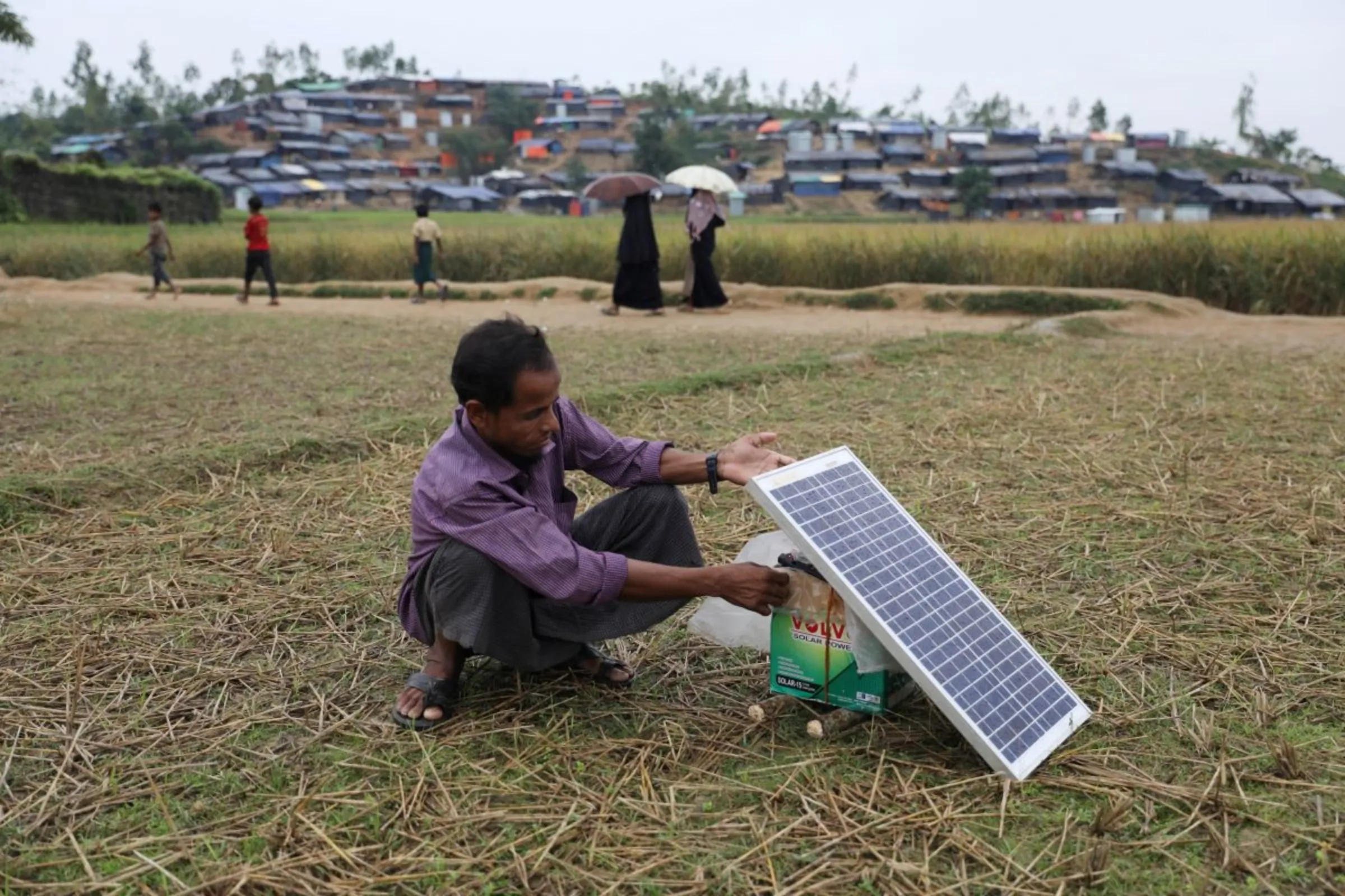 A Rohingya refugee man charges his mobile phone from a solar panel in the Palong Khali refugee camp in Cox's Bazar, Bangladesh, November 17, 2017