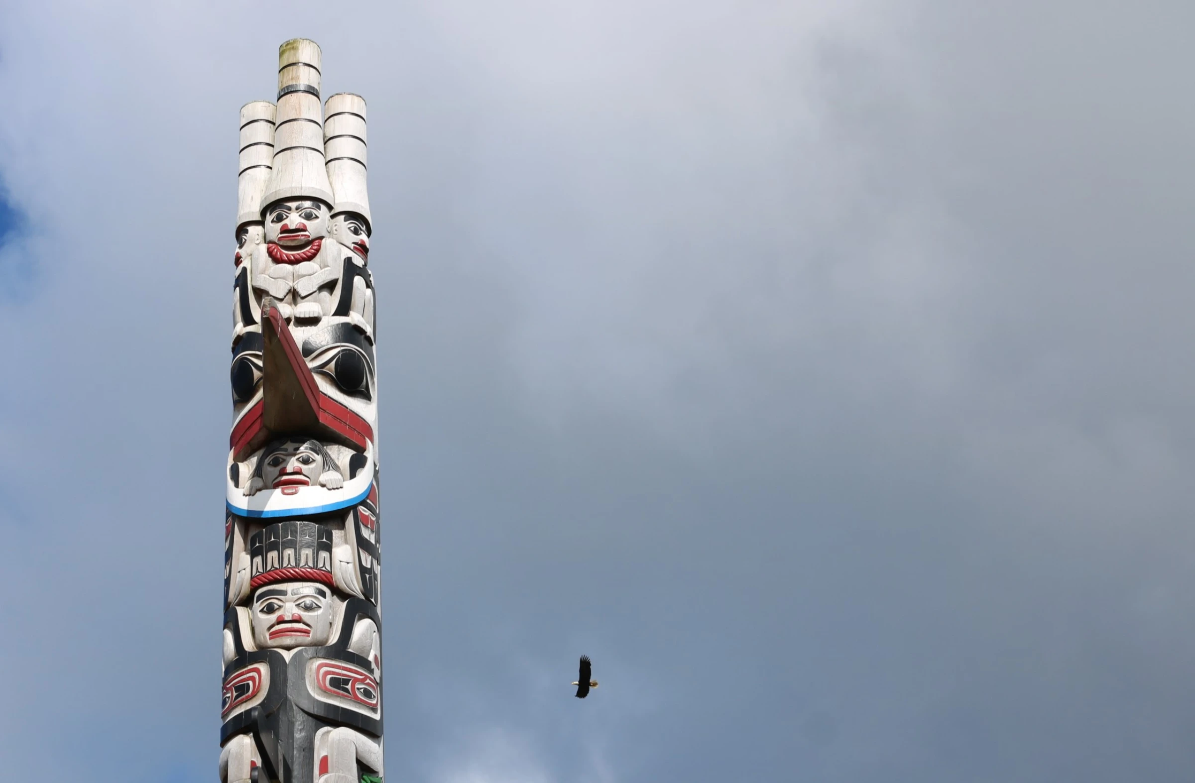 An eagle flies past a totem pole carved by Haida carver Christian White in Old Massett, in the north of Haida Gwaii on Graham Island, Canada. July 23, 2024. Thomson Reuters Foundation/Jack Graham