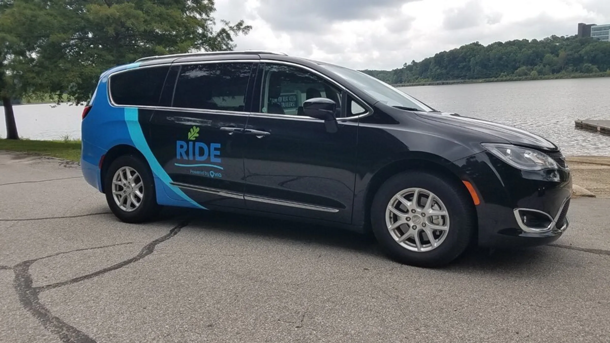 An on-demand transit car is parked in front of a lake