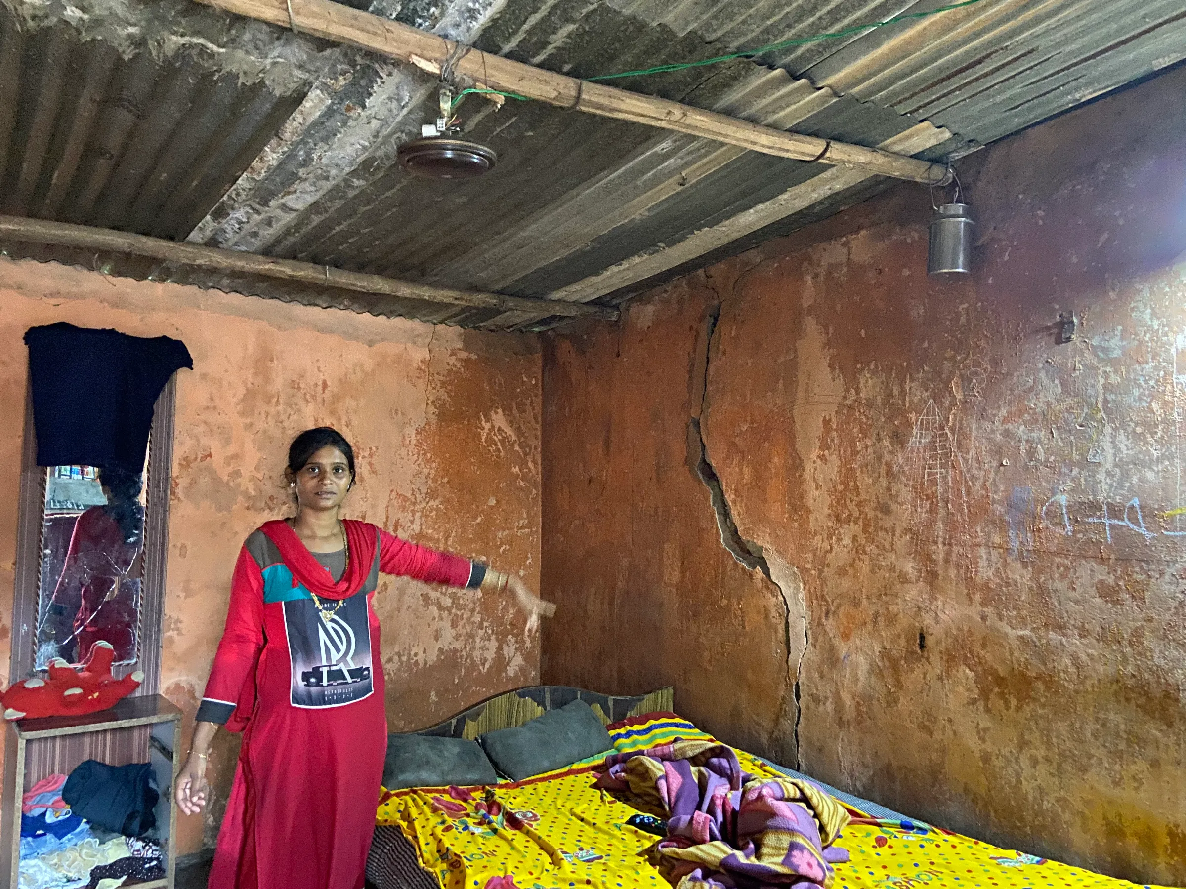 A woman points at a large crack in the wall in her home