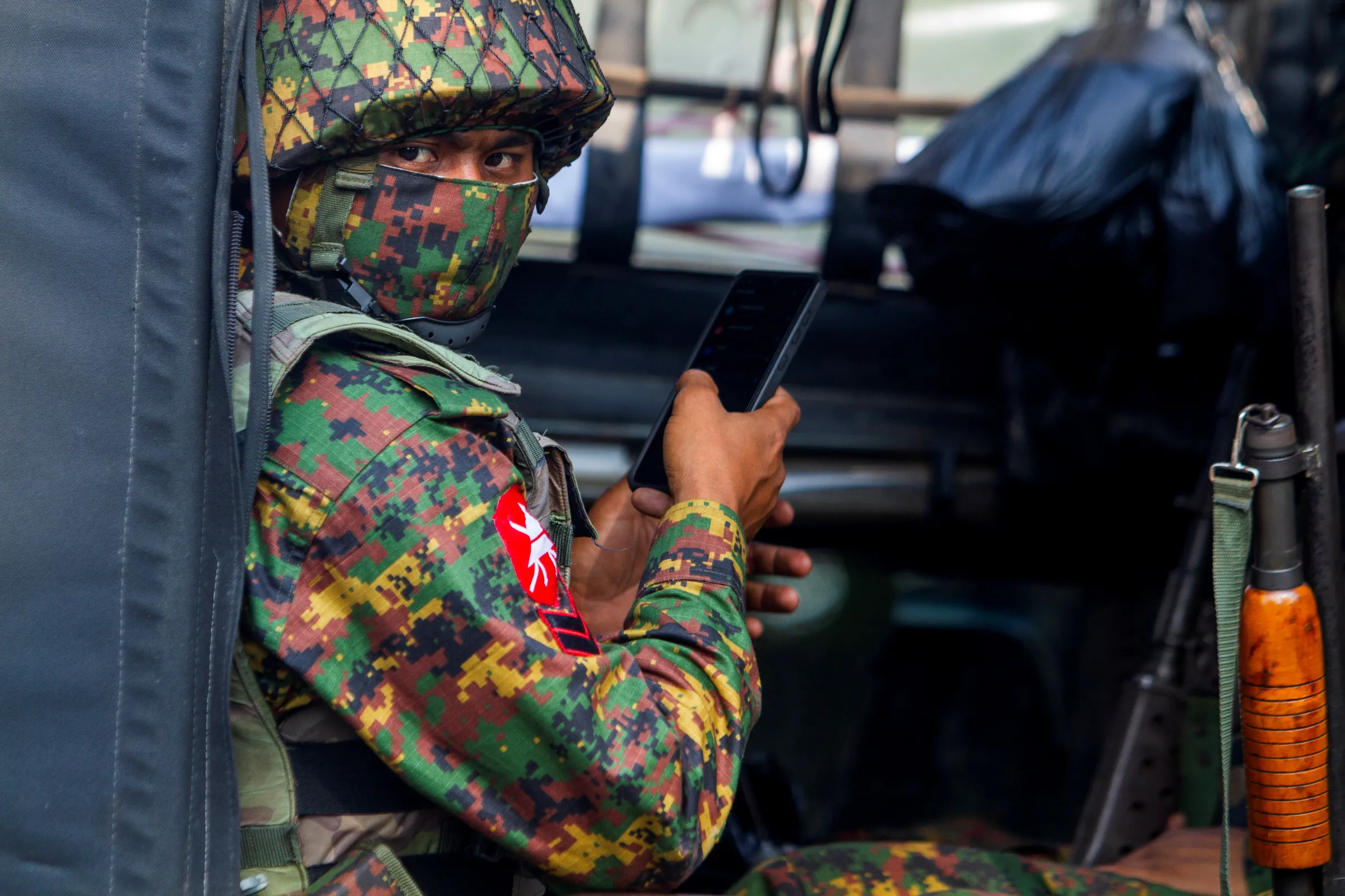 A soldier uses a mobile phone as he sit inside a military vehicle outside Myanmar's Central Bank during a protest against the military coup, in Yangon, Myanmar, February 15, 2021. REUTERS/Stringer