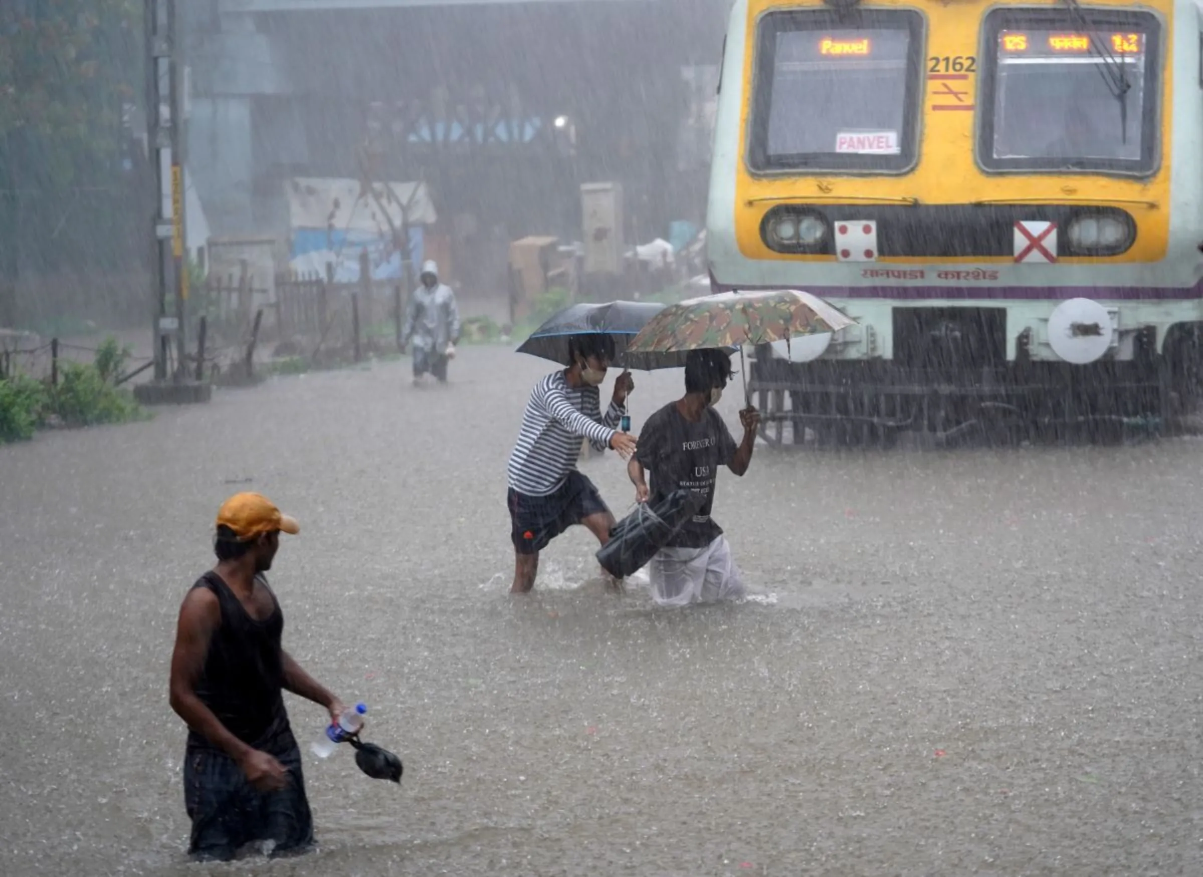People cross waterlogged railway tracks next to a parked passenger train during heavy rains in Mumbai, India, June 9, 2021. REUTERS/Hemanshi Kamani