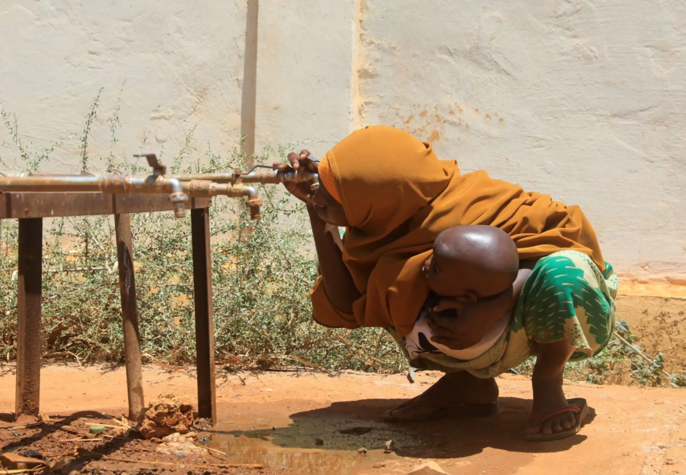 An internally displaced Somali woman holds her child as she drinks water from a tap outside the feeding centre, a new site for IDPs, in Barwaaqo, near Baidoa, Somalia, February 21, 2023