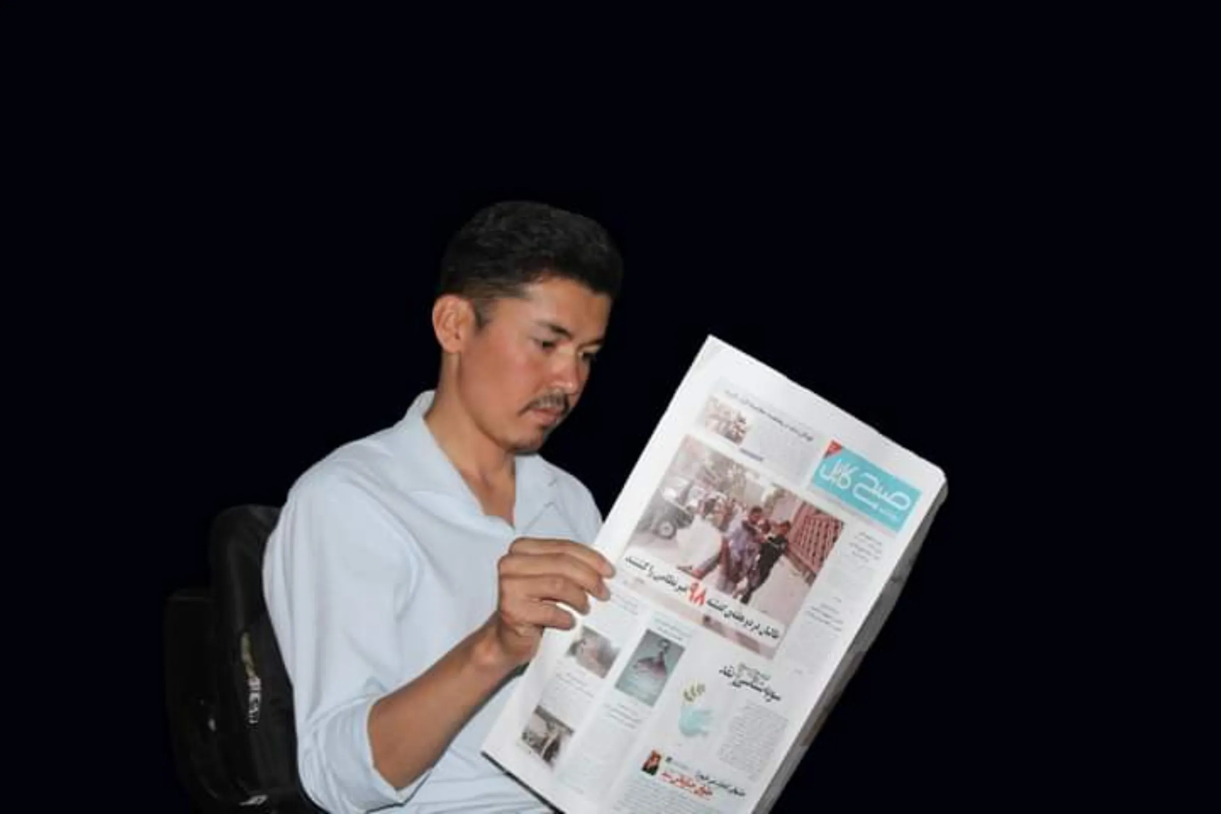 Afghan journalist Ismail Lali is seen in Kabul holding a newspaper in the dark