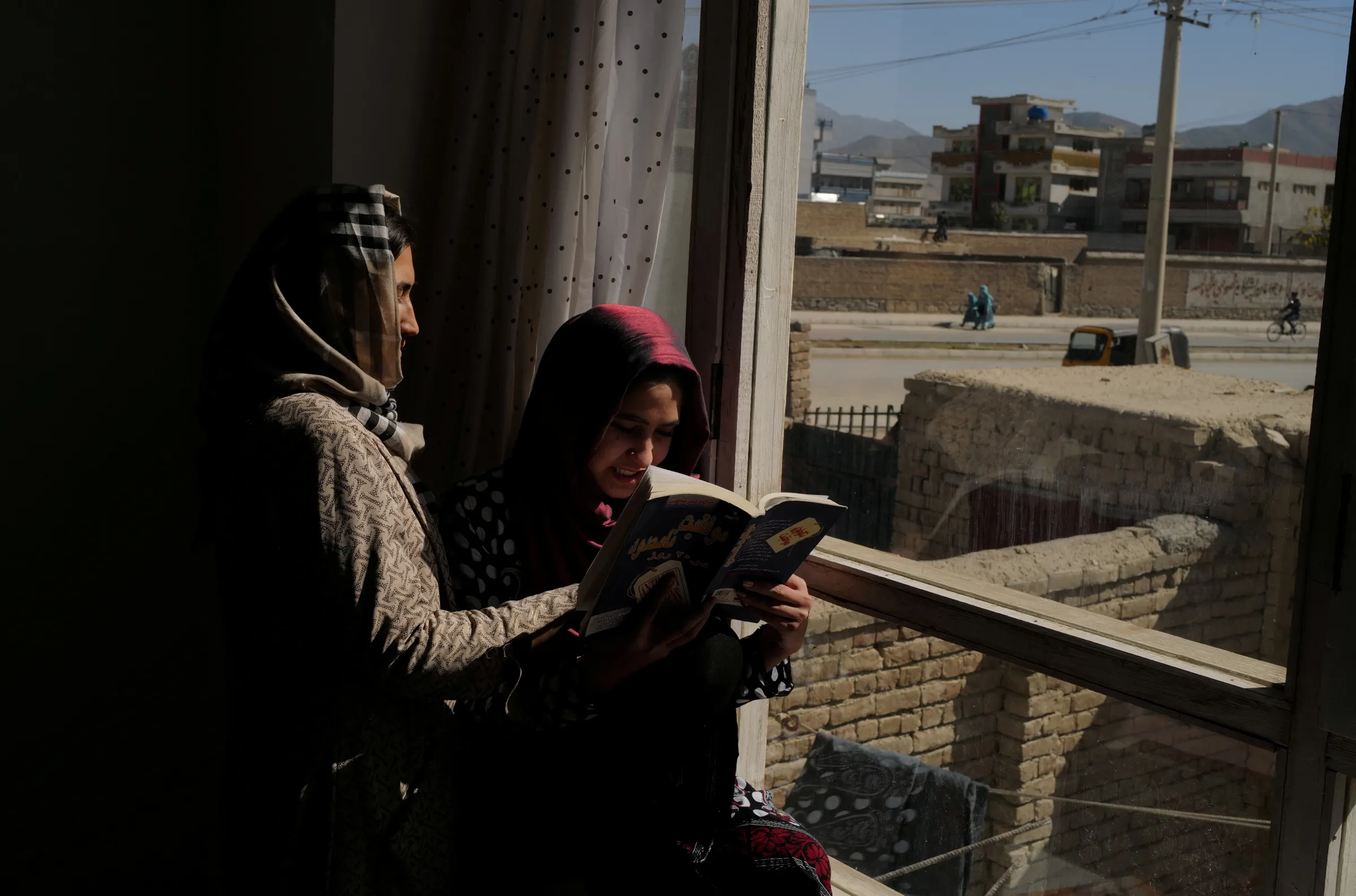 A student reads a book with her sister on a windowsill at their home in Kabul, Afghanistan, October 23, 2021