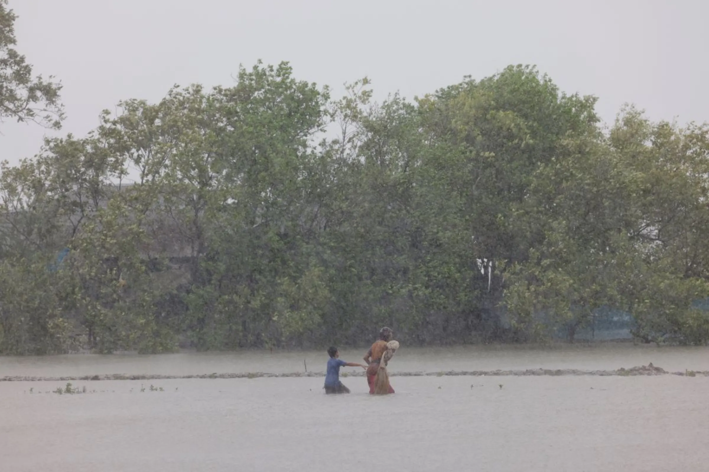 A woman and child wade through water as Cyclone Remal hits Bangladesh, May 27, 2024. REUTERS/Mohammad Ponir Hossain