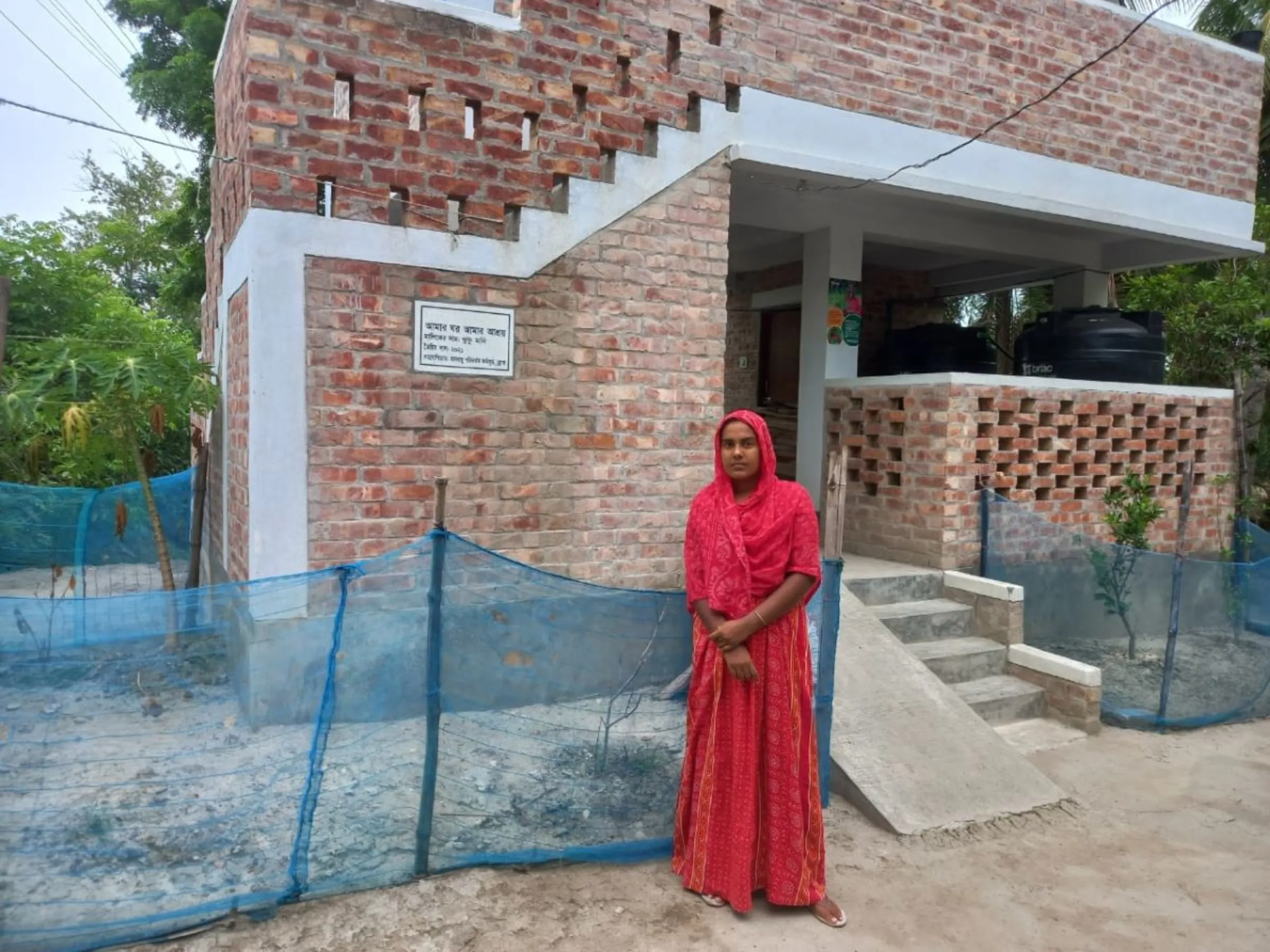 Khuku Moni, 35, poses before her house built with the support of the development organisation BRAC that protects her family as well as her neighbours from seasonal storms, June 8, 2023