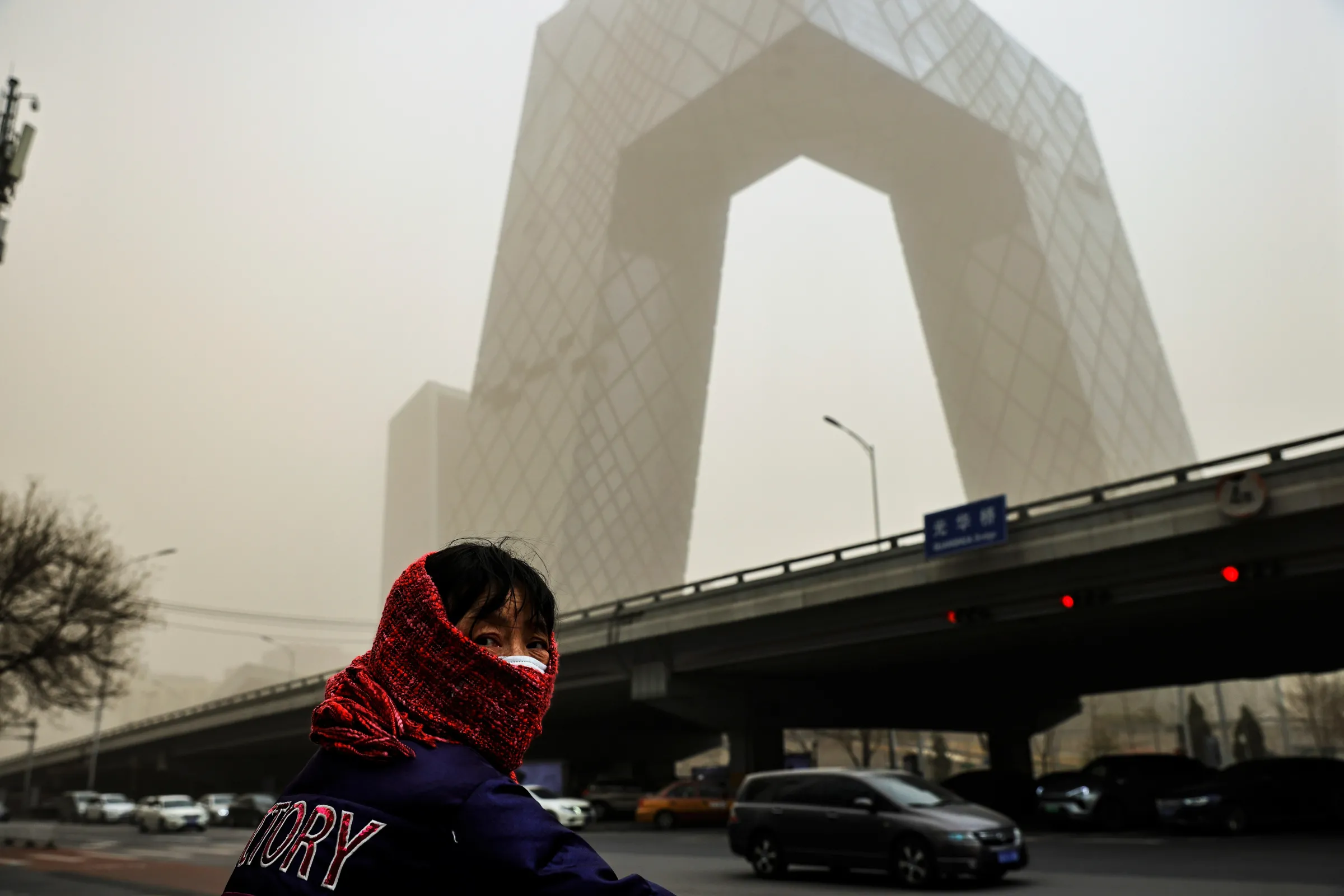 A woman wearing a head covering is seen in front of the headquarters of China's state media broadcaster CCTV that is shrouded in haze after a sandstorm