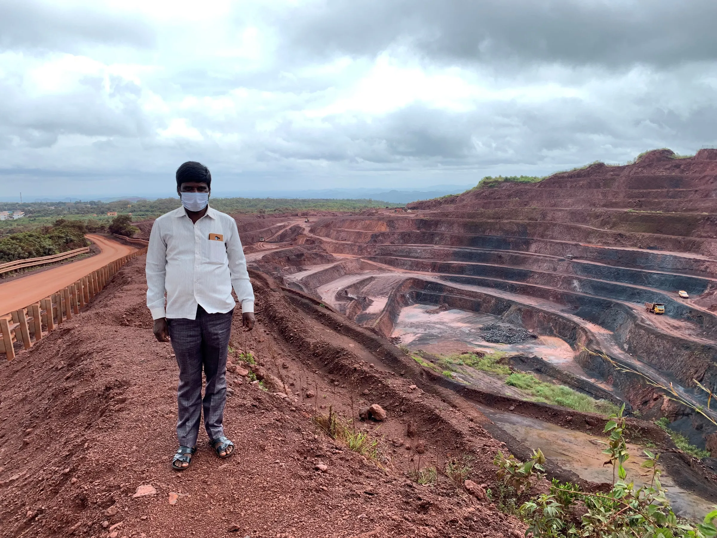 A man wearing a face mask stands above an open cast mine