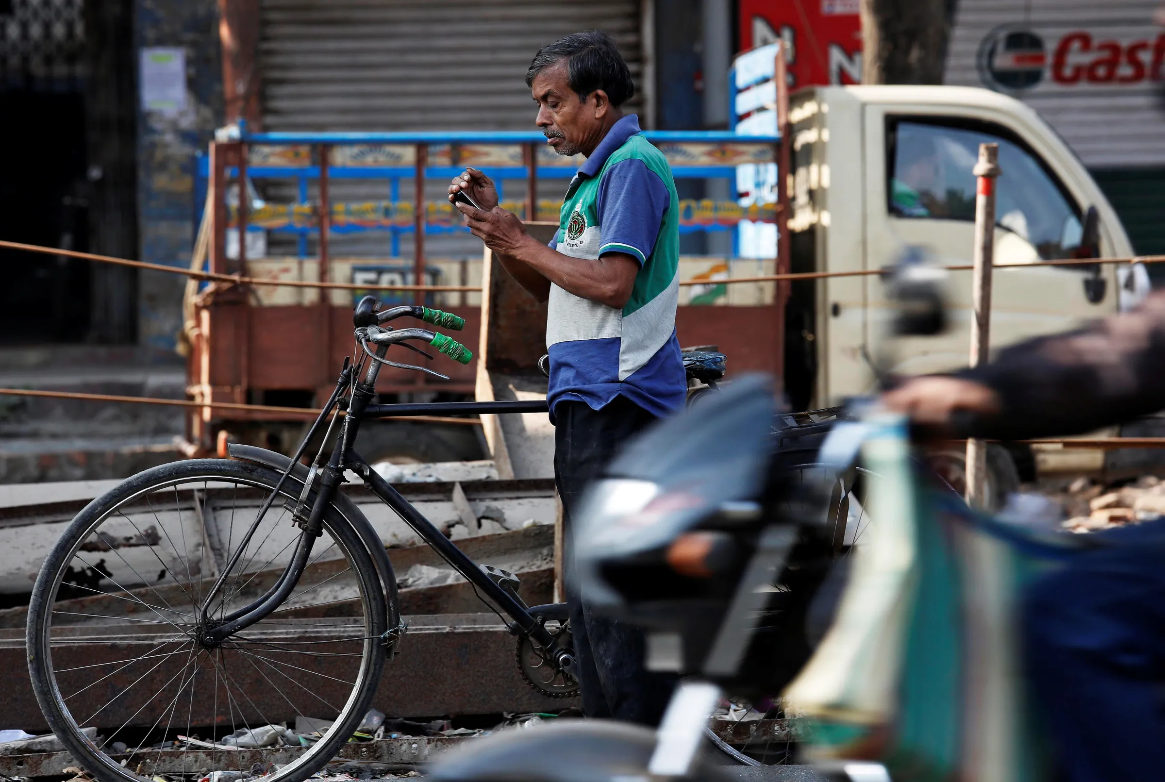 A man with a bike checks his mobile phone as he stands on a busy road in Kolkata, Indi