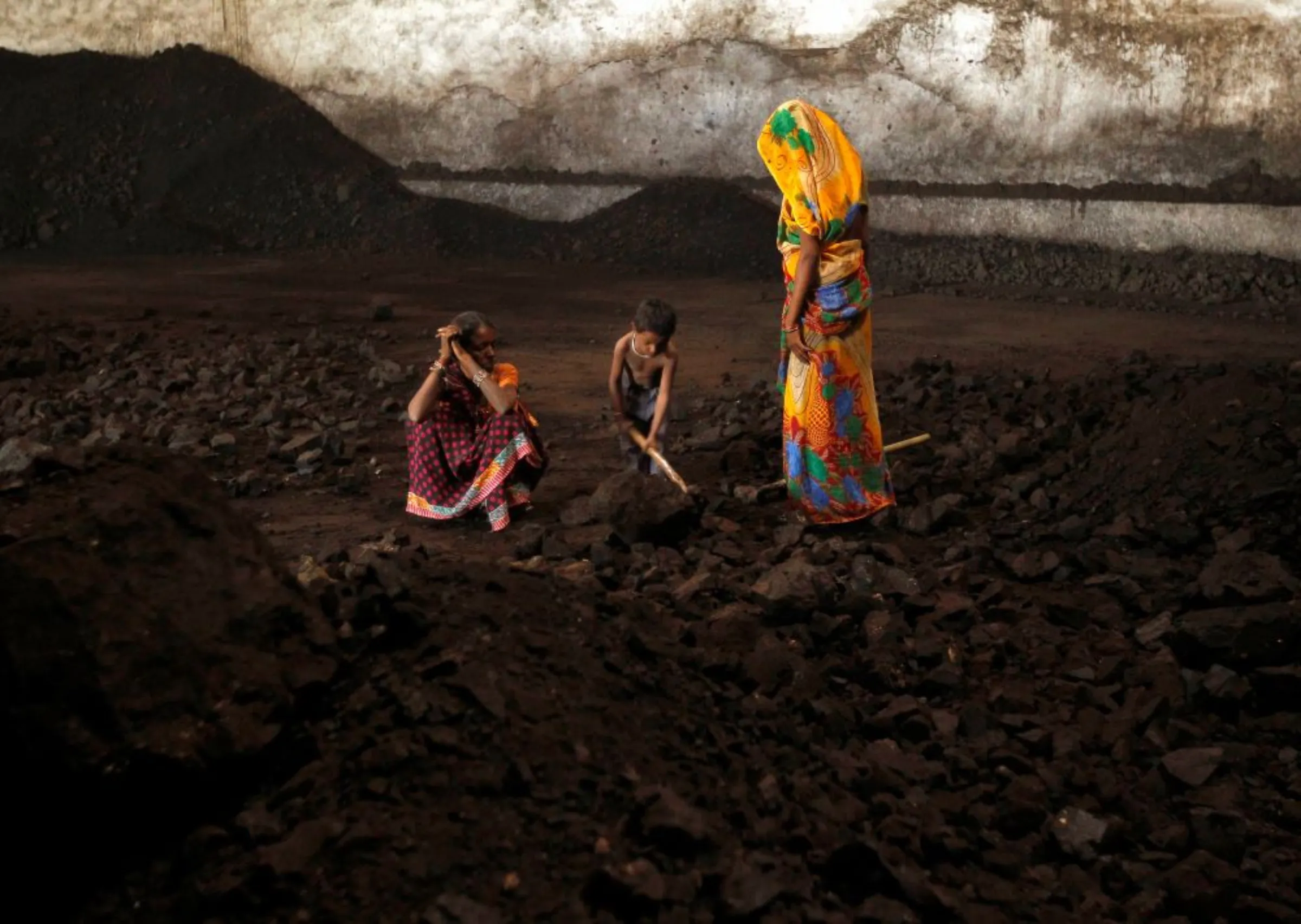 Labourers rest as a boy playfully shovels coal at a yard in the western Indian city of Ahmedabad November 20, 2014