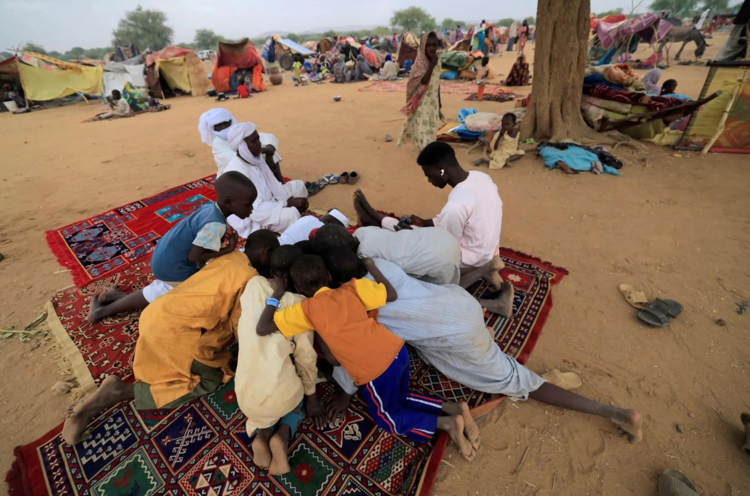 Sudanese refugee children who have fled the violence in Sudan's Darfur region, play a game on a mobile phone beside makeshift shelters, near the border between Sudan and Chad in Koufroun, Chad May 11, 2023
