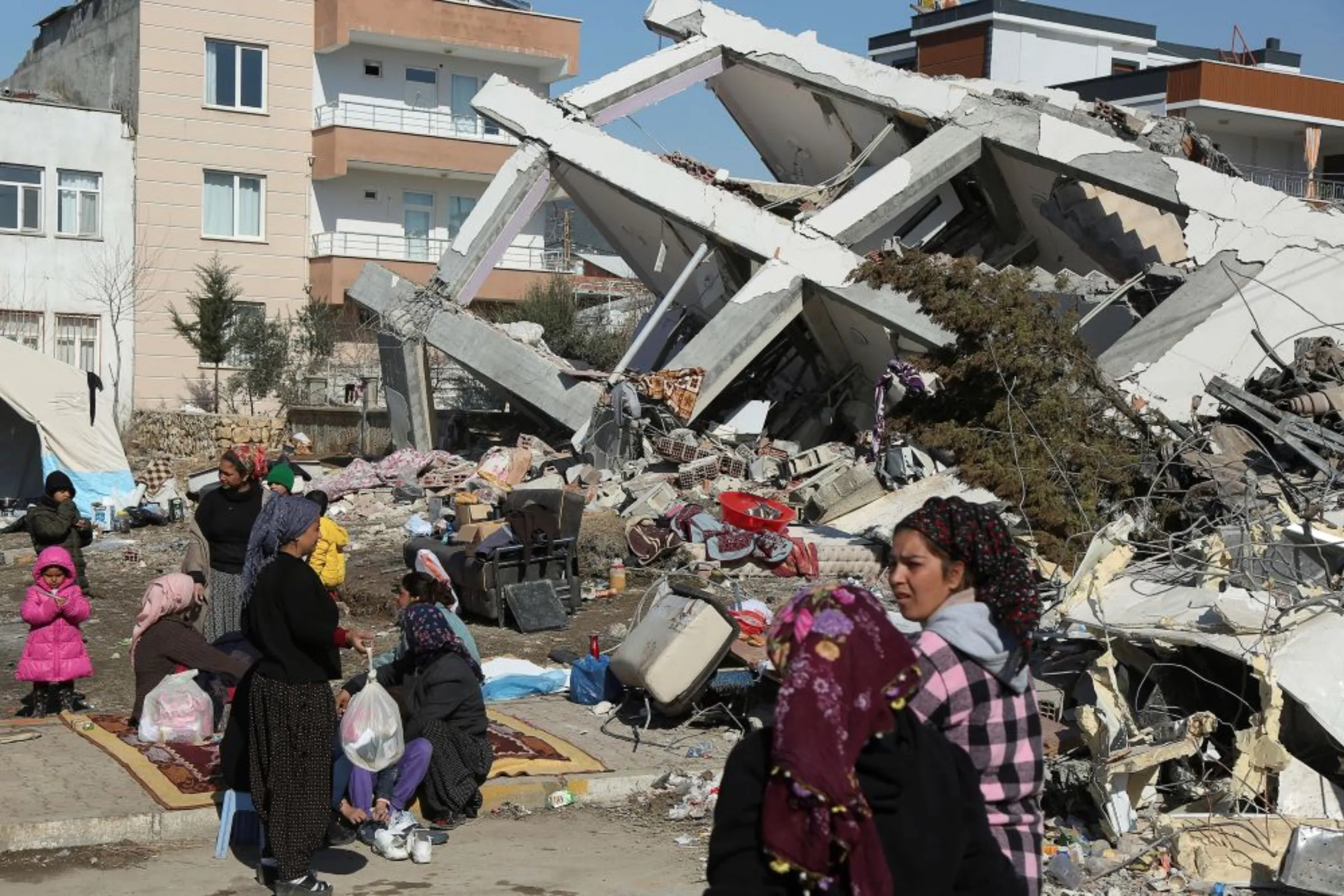 People sit and stand near a collapsed building, in the aftermath of the deadly earthquake, in Adiyaman, Turkey, February 12, 2023