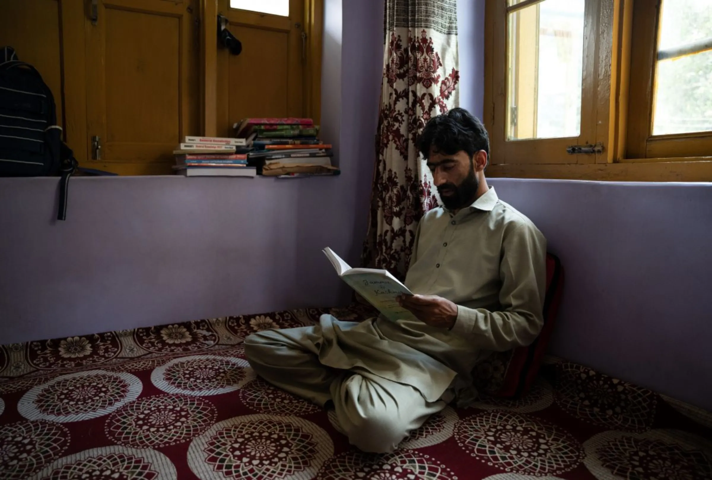 Ayaz Nabi Malik reads at his home in Pulwama district, South Kashmir. August 25, 2024. Thomson Reuters Foundation/Mehran Firdous.