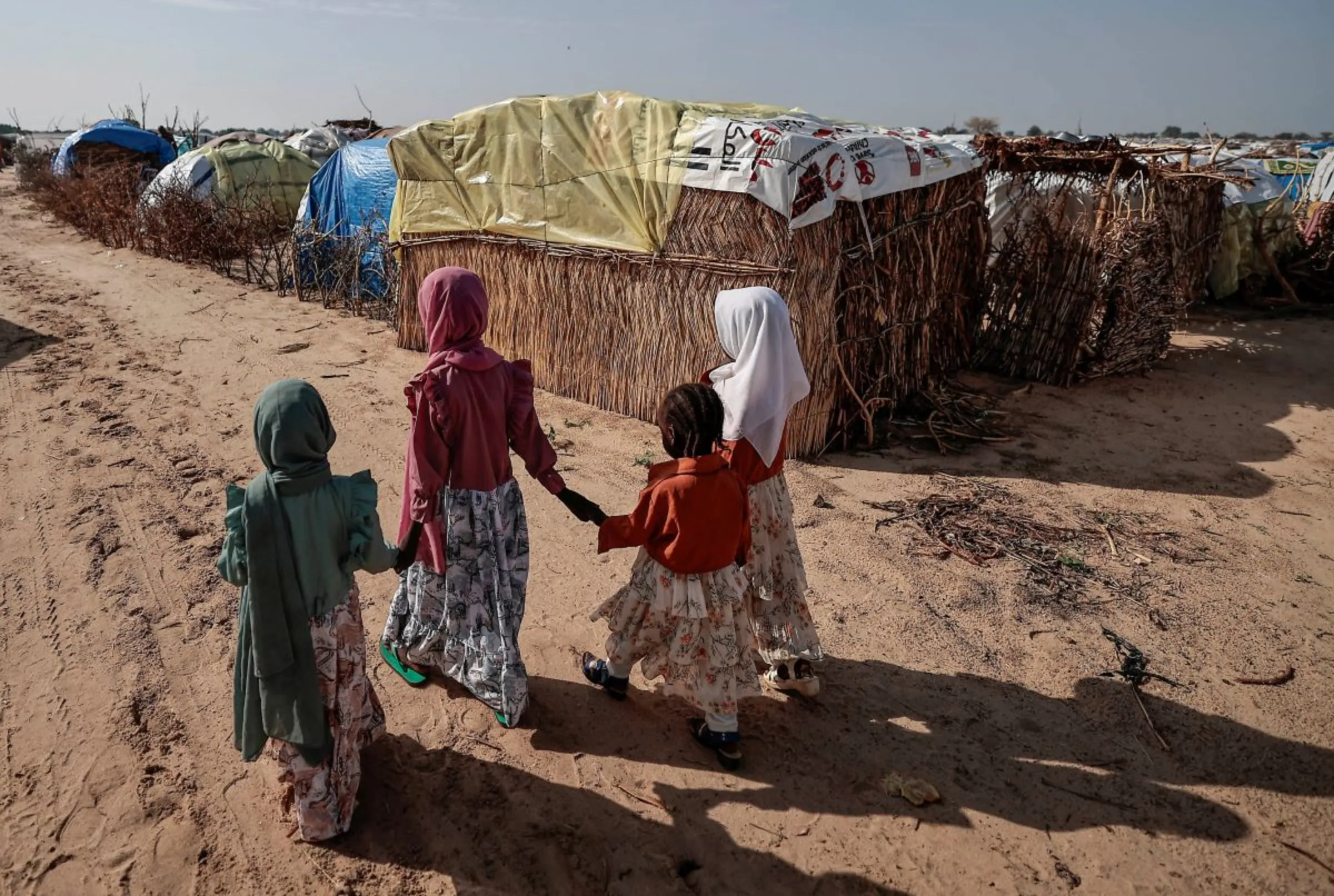 Sudanese girls who fled the conflict in Sudan's Darfur region, walk beside makeshift shelters holding each other's hands in Adre, Chad July 29, 2023