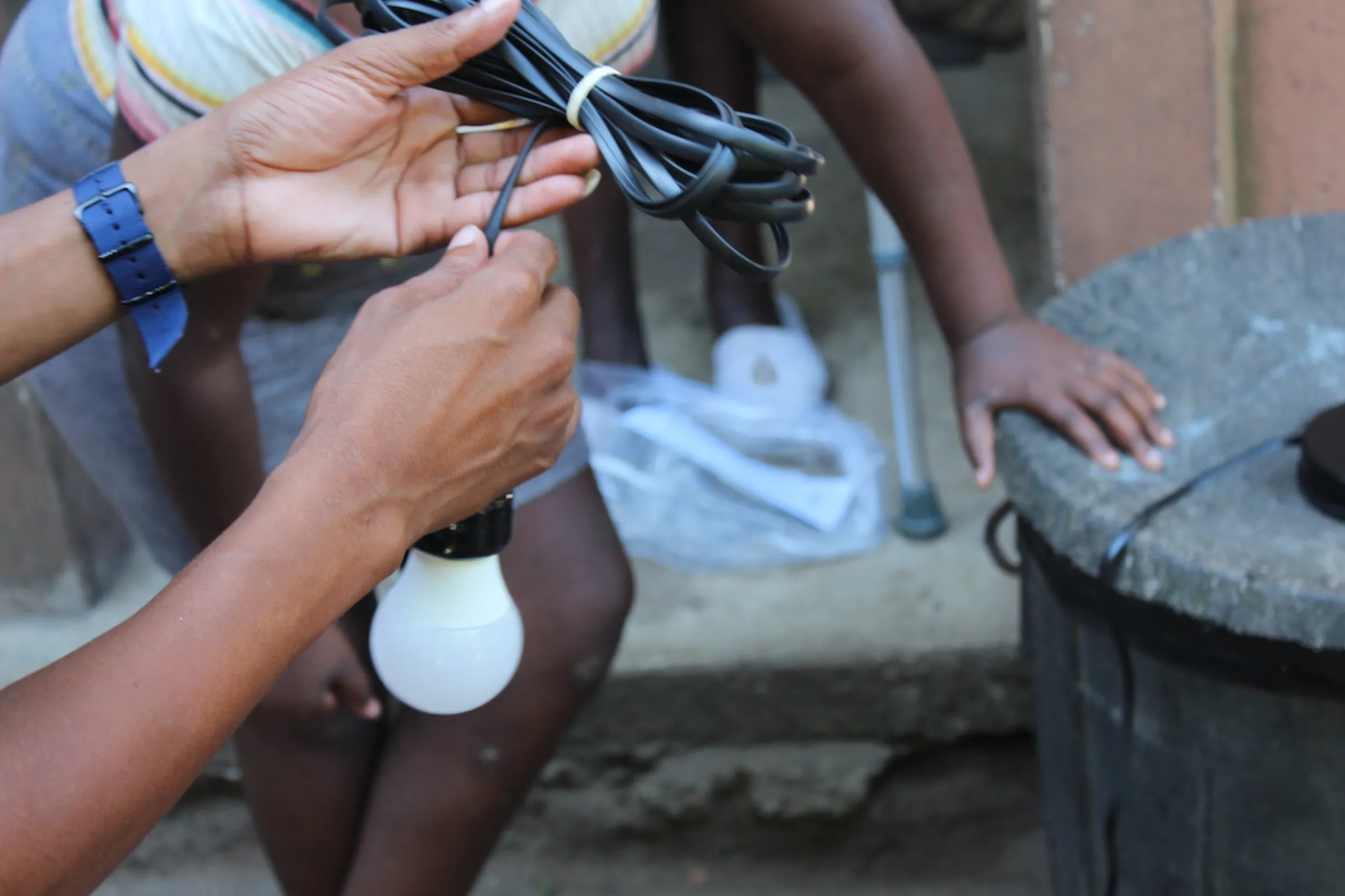 The team at Light Up A Home (LUAH) helps connect a lightbulb to their solar panel device in Sheffield Informal Settlements KwaDukuza, KwaZulu-Natal, South Africa January 2021. Balwin Foundation/Handout via Thomson Reuters Foundation