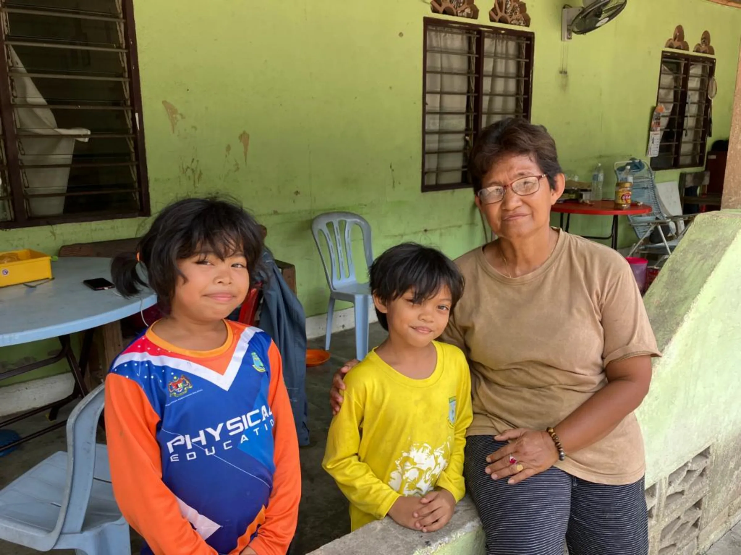 Reta Lajah, an indigenous palm oil farmer poses with two of her grandchildren outside her home in the village of Sungai Judah, Selangor, Malaysia, March 30, 2023. Thomson Reuters Foundation/Michael Taylor