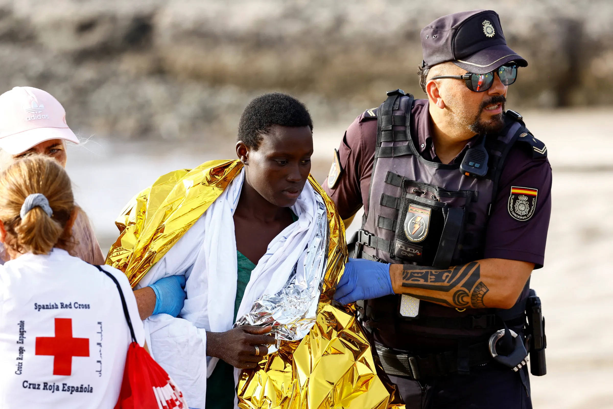 A police officer, together with members of the Red Cross, assist a migrant woman after she arrived with others in a fiber boat at Las Burras beach in San Agustin, on the island of Gran Canaria, Spain, July 19, 2024. REUTERS/Borja Suarez