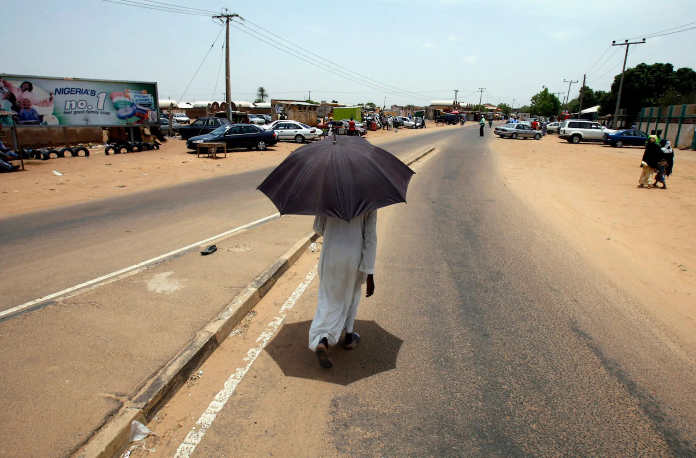 A man protects himself from the scorching sun with an umbrella as he walks on a street in Kano April 22, 2007. REUTERS/Radu Sigheti