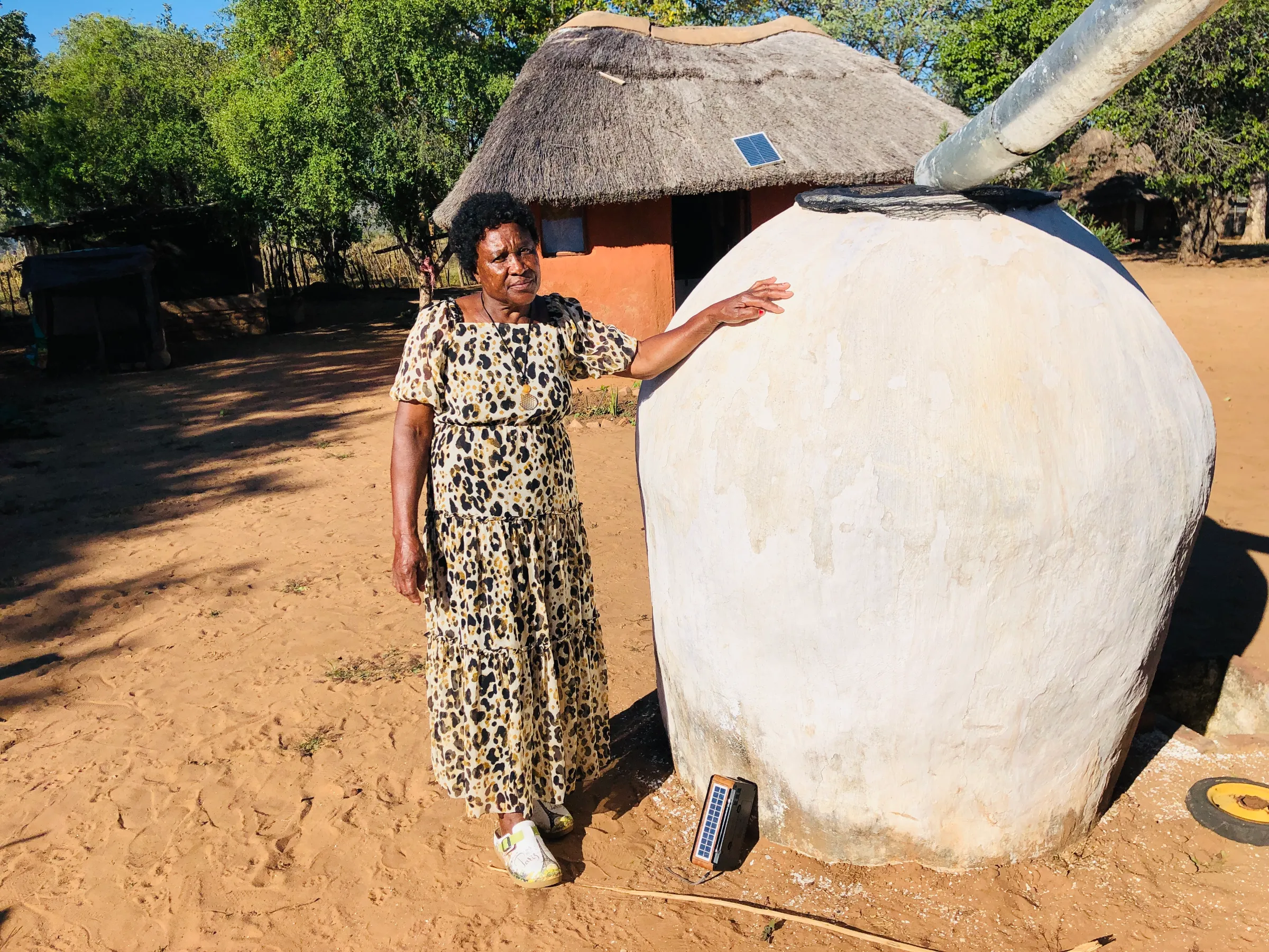 Constance Ndaba poses next to a giant rainwater harvesting jar at her home in Masikili Village 2. The jar helps her family cope with water shortages when nearby boreholes and rivers run dry. 7 May 2025. Lungelo Ndhlovu/Thomson Reuters Foundation.