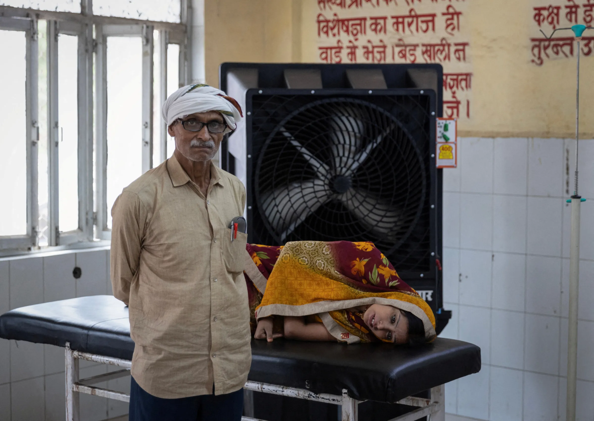 A woman suffering from heat-related illness lies on a stretcher with her father next to her at a hospital in Ballia District, Uttar Pradesh, India, June 21, 2023. REUTERS/Adnan Abidi