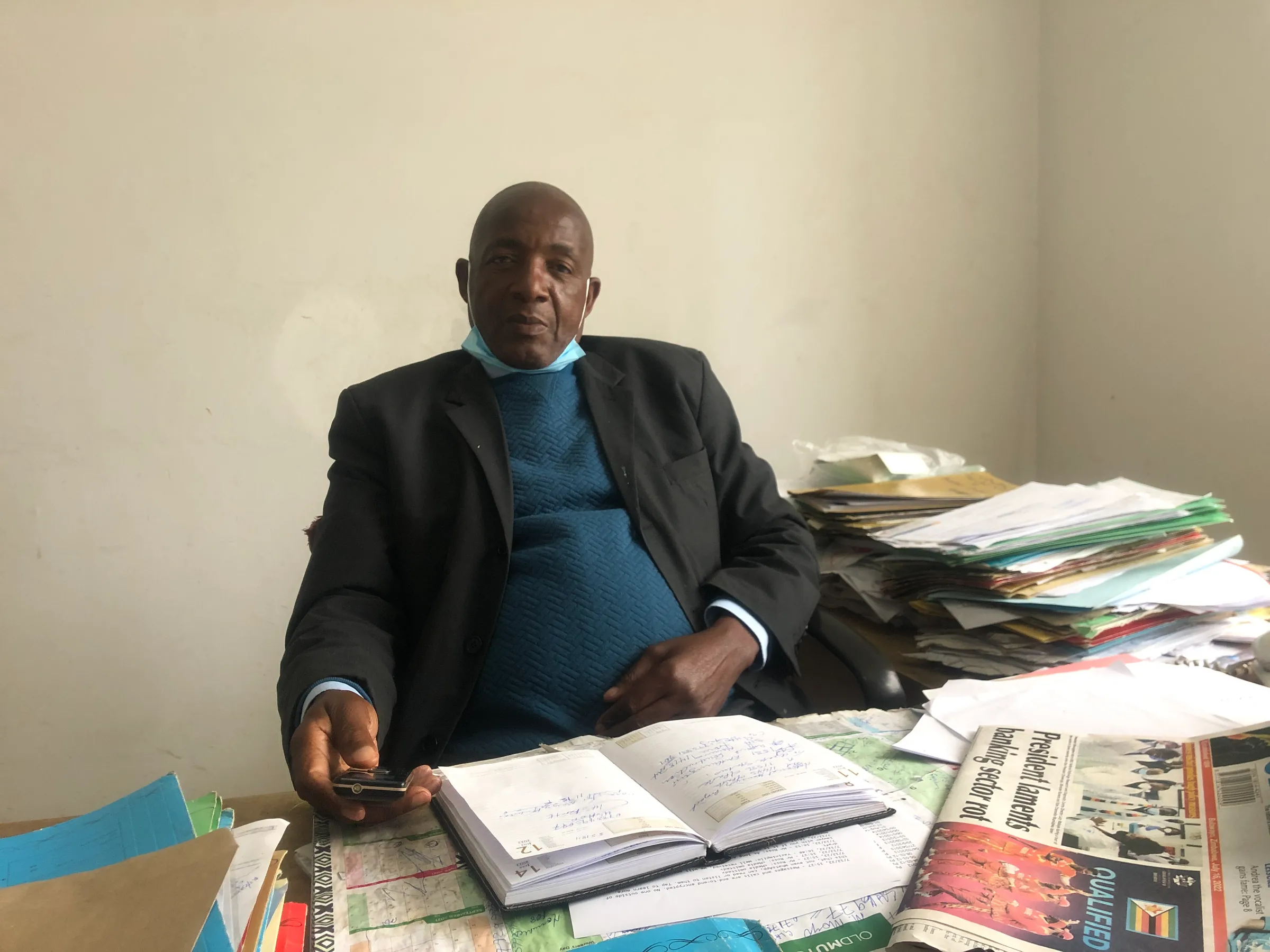 A man sits at a desk covered with open books and documents