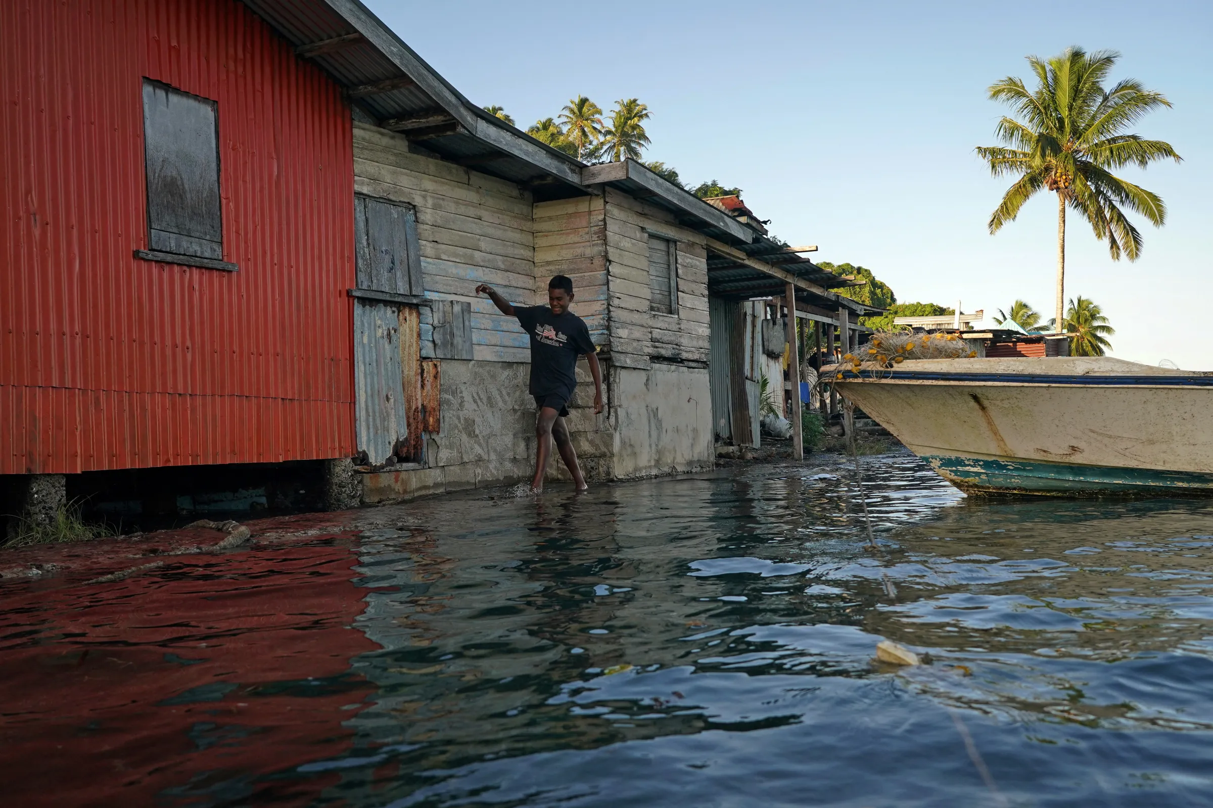 Local boy wades through seawater flooding over an ineffective sea wall at high tide, as the community experiences flooding in Serua Village, Fiji, July 15, 2022. REUTERS/Loren Elliott