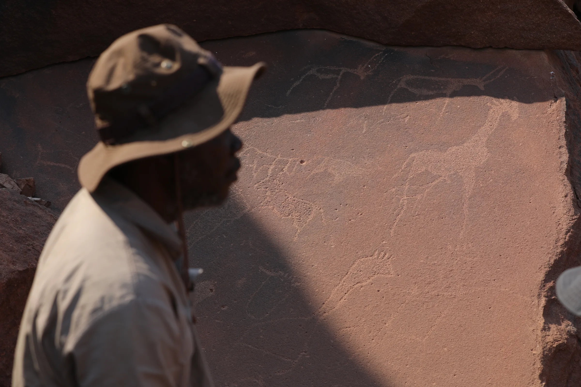 Guide Raymond Geiseb stands in front of a rock lit up by sunshine that displays rock art engravings at Twyfelfontein heritage site in Namibia, September 29, 2022