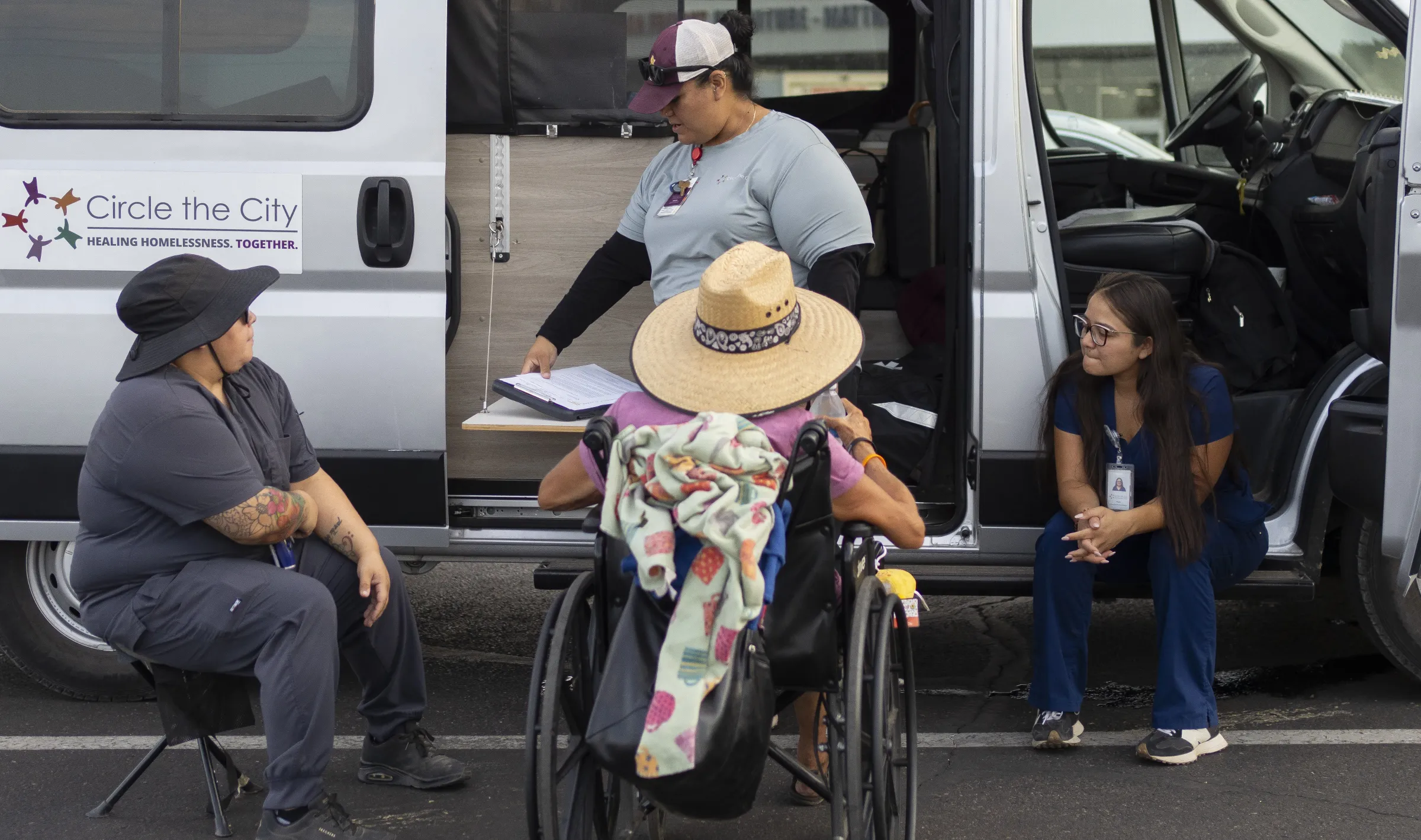 From left, Circle the City staff, Maritza Arias, Brenda Madril and Perla Puebla examine Maurajean Bunn in Phoenix, Arizona. July 15, 2024. Thomson Reuters Foundation/Rebecca Noble