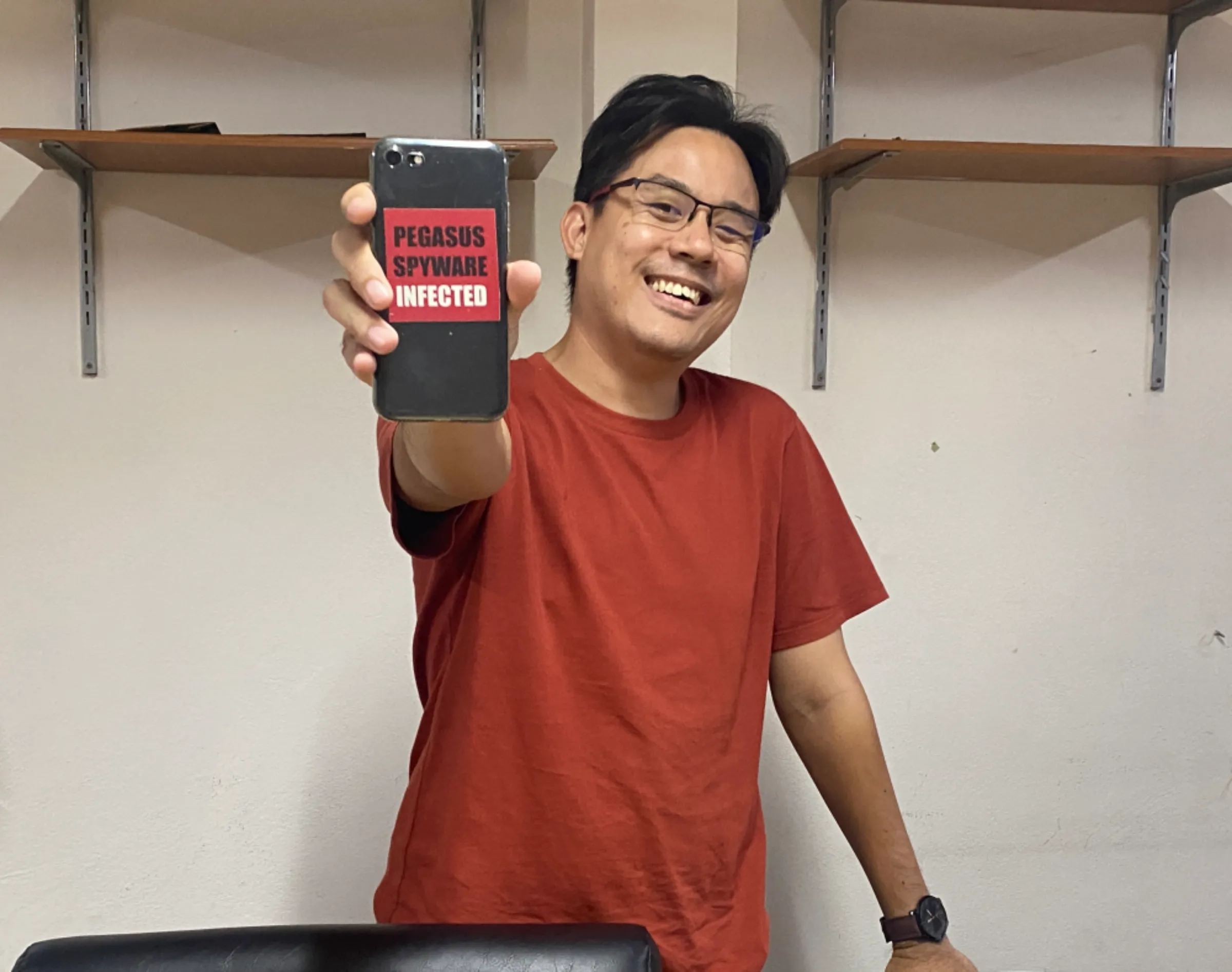 Yingcheep Atchanont, a lawyer at legal non-profit iLaw, holds up his mobile phone with a sticker reading 'Pegasus spyware infected' in his office in Bangkok, Thailand. January 12, 2023