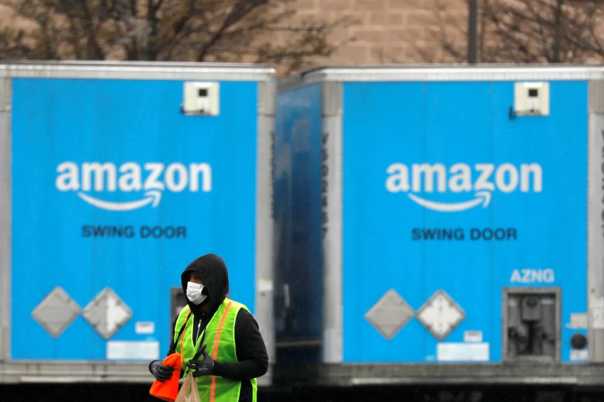 A worker in a face mask walks by trucks parked at an Amazon facility as the global coronavirus outbreak continued in Bethpage on Long Island in New York, U.S., March 17, 2020. REUTERS/Andrew Kelly