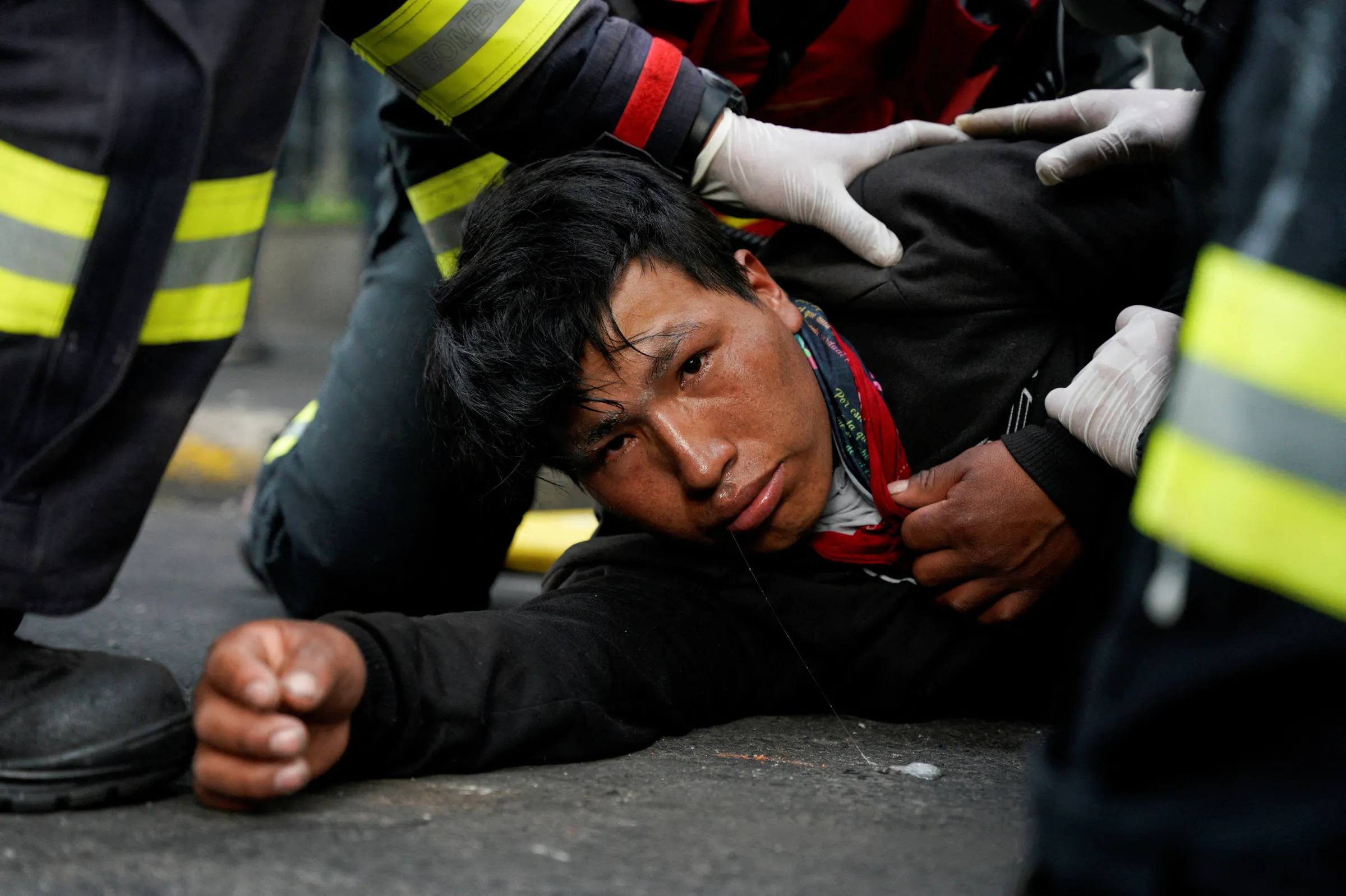 A man lying on the road with his arm stretched out towards the camera is seen to by medical staff wearing uniform