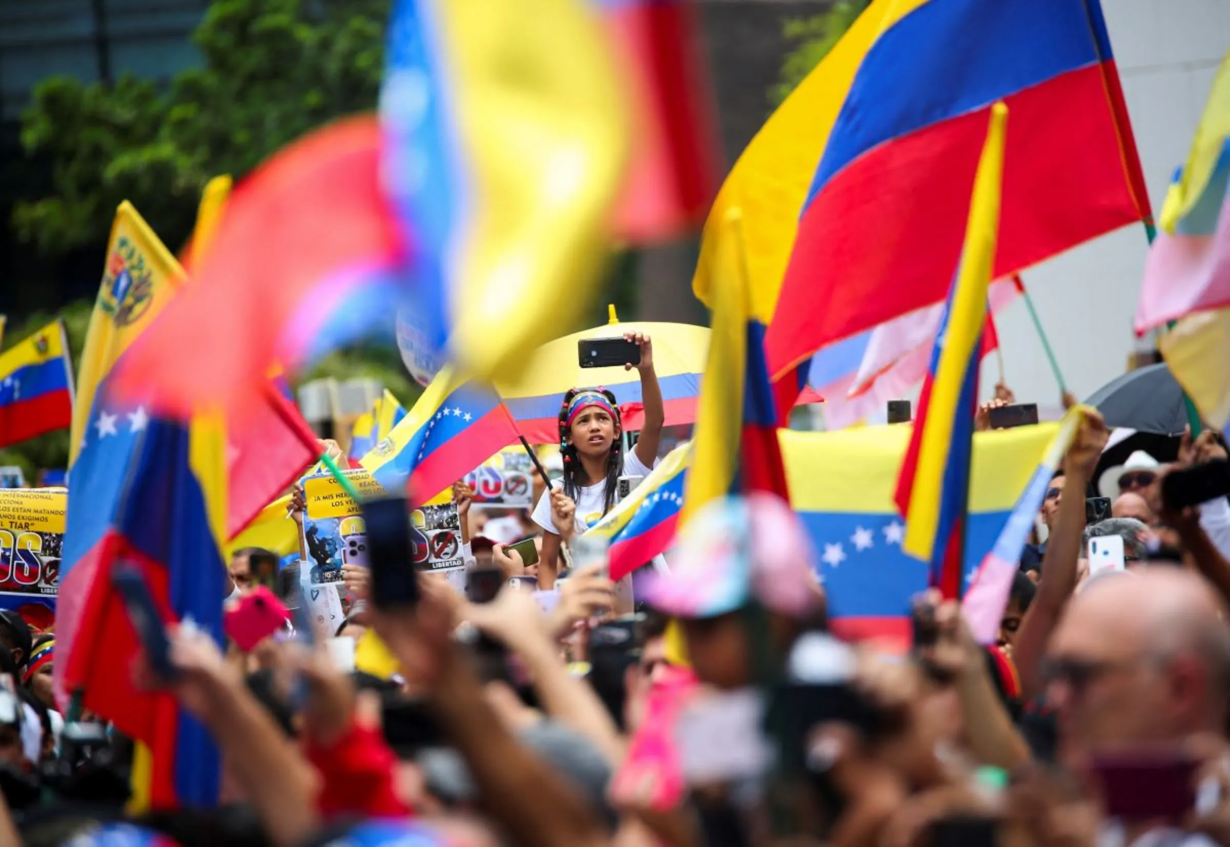 A girl uses a mobile phone as Venezuelans living in Colombia wave Venezuela's national flags during a protest against election results, in Medellin, Colombia August 7, 2024. REUTERS/Juan David Duque