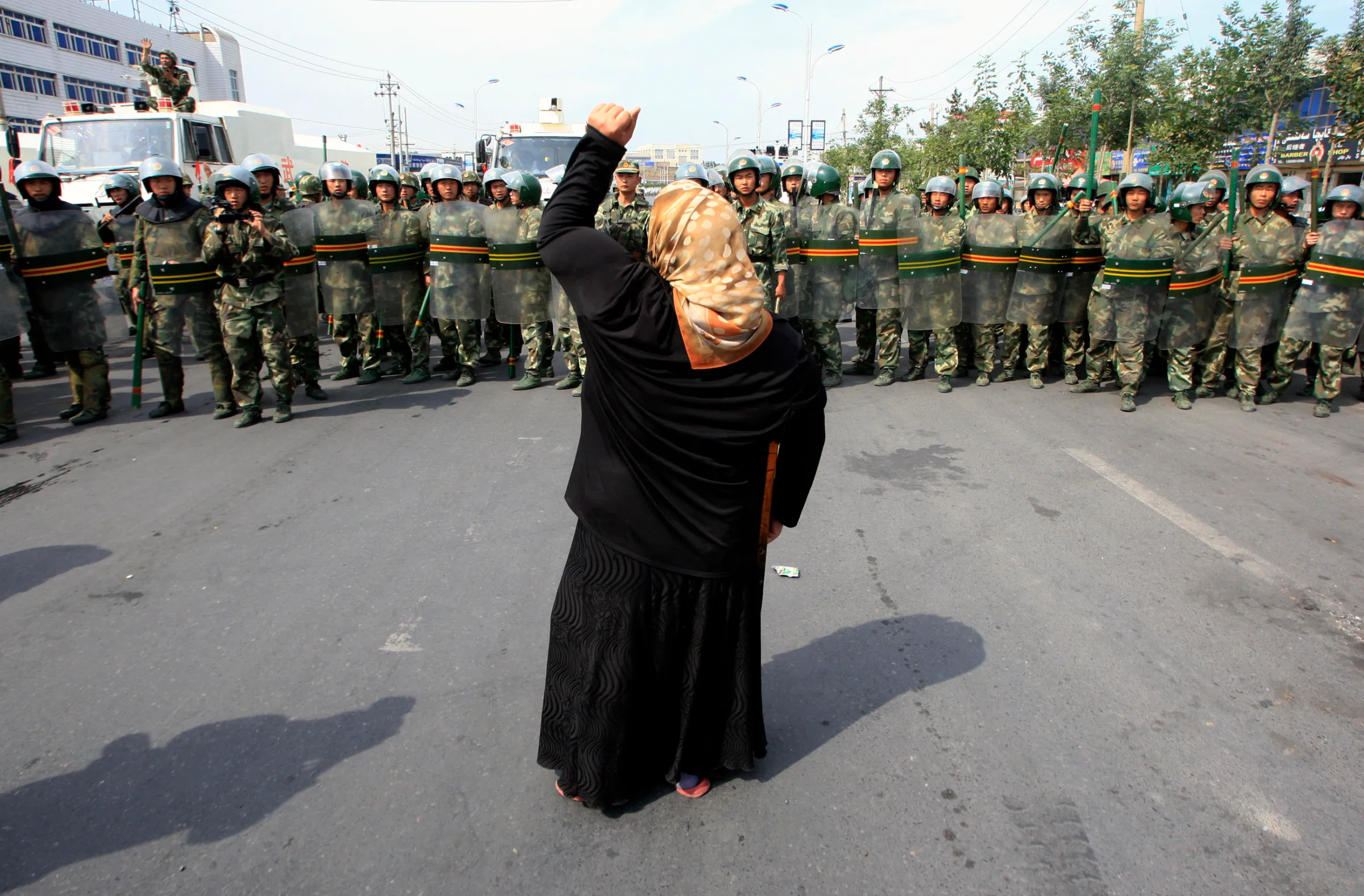 A local woman on a crutch shouts at Chinese paramilitary police wearing riot gear as a crowd of angry locals confront security forces on a street in the city of Urumqi in China's Xinjiang Autonomous Region