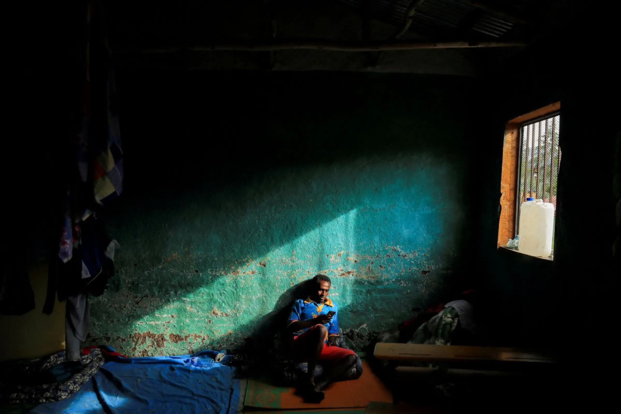 A man browses with his phone in his shelter at a camp for the internally displaced due to the fighting between the Ethiopian National Defense Force (ENDF) and the Tigray People's Liberation Front (TPLF) forces in Dessie town, Amhara Region, Ethiopia, October 8, 2021
