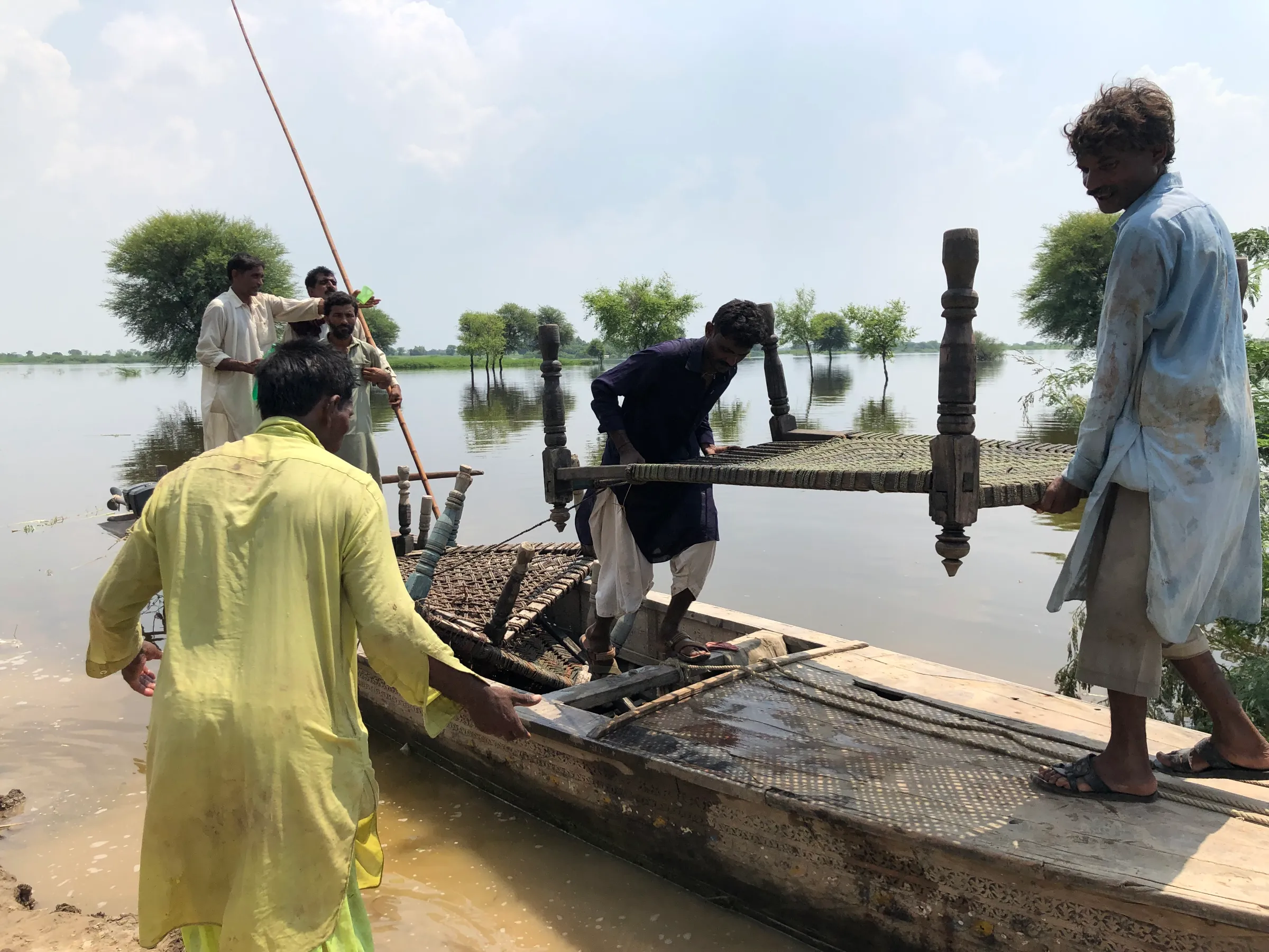 Flood-affected displaced people retrieve charpais (rope beds) from their submerged homes in the village of Jerrar Bheel, in Pakistan, September 10, 2022. Thomson Reuters Foundation/Zofeen Ebrahim