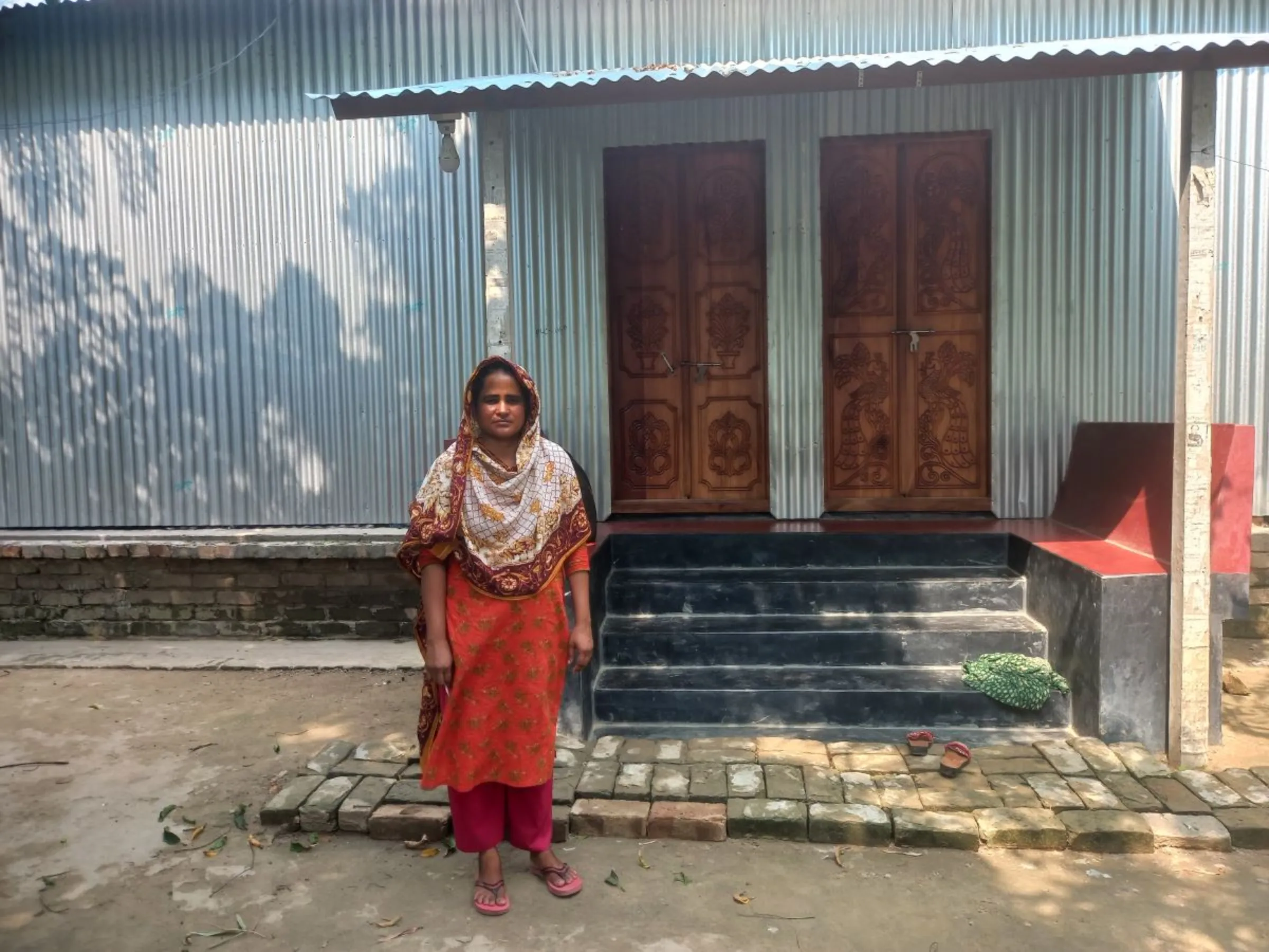 Salma Akhtar, a farmer from Faridpur who works as a volunteer for the flood resilience programme of Practical Action, poses for a picture in front of her house with a raised plinth, May 21, 2023