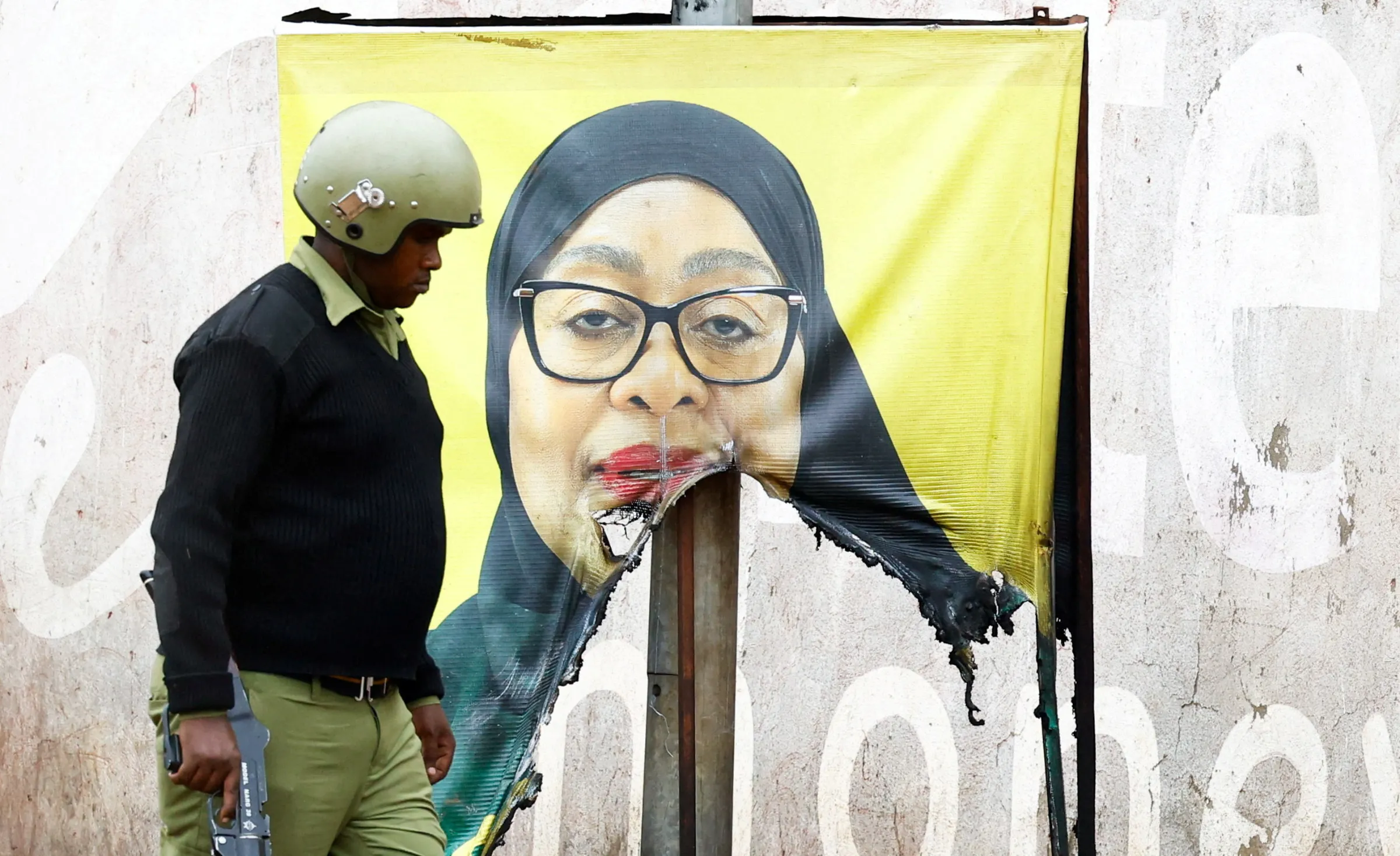 A Tanzanian riot police officer walks past a vandalised campaign poster of President Samia Suluhu Hassan, following a protest a day after a general election marred by violent demonstrations over the exclusion of two leading opposition candidates at the Namanga One-Post Border crossing point between Kenya and Tanzania, October 30, 2025. REUTERS/Thomas Mukoya TPX IMAGES OF THE DAY