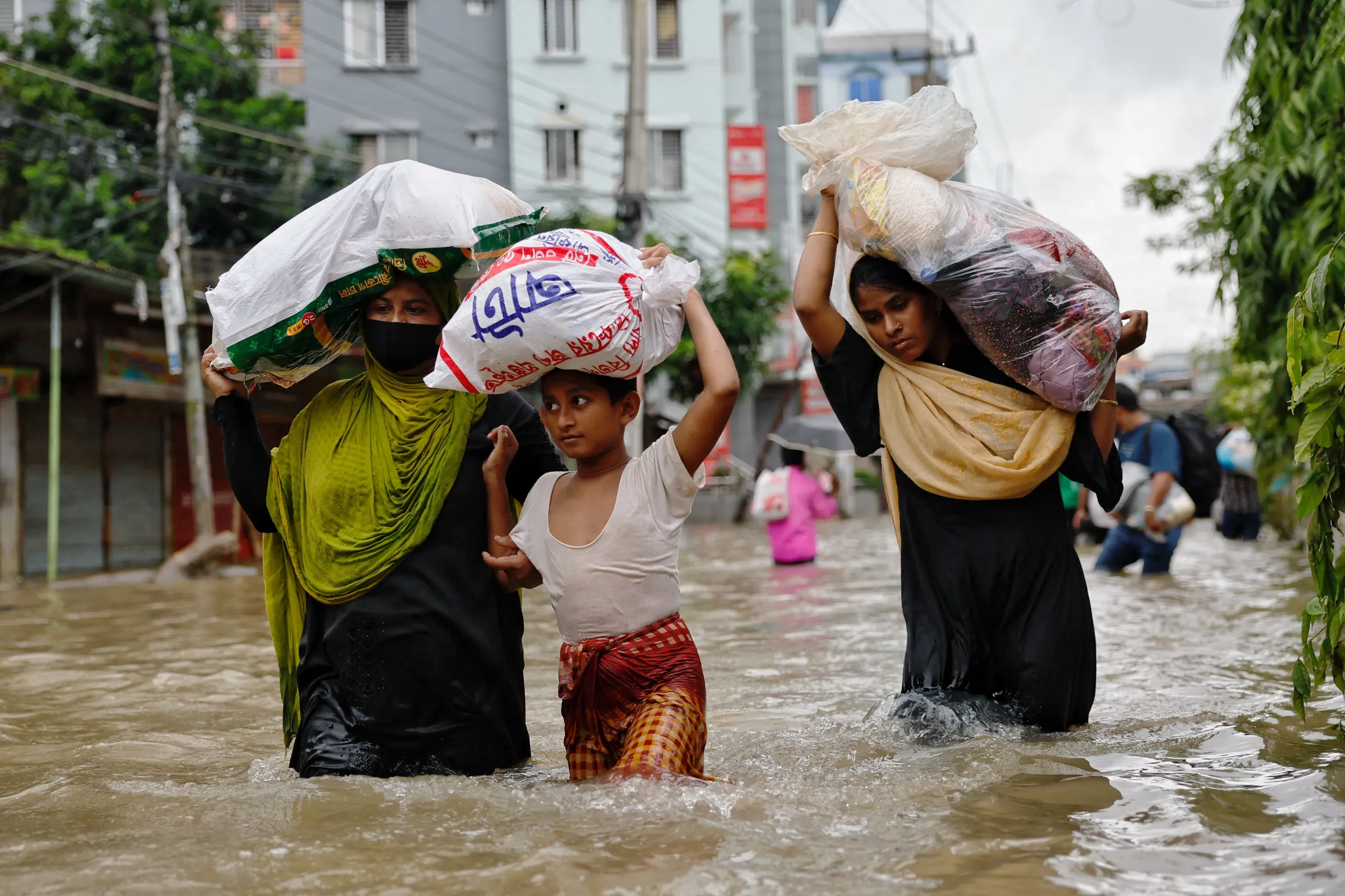 People wade through water as they carry relief supplies amid severe flooding in Feni, Bangladesh, August 25, 2024. REUTERS/Mohammad Ponir Hossain