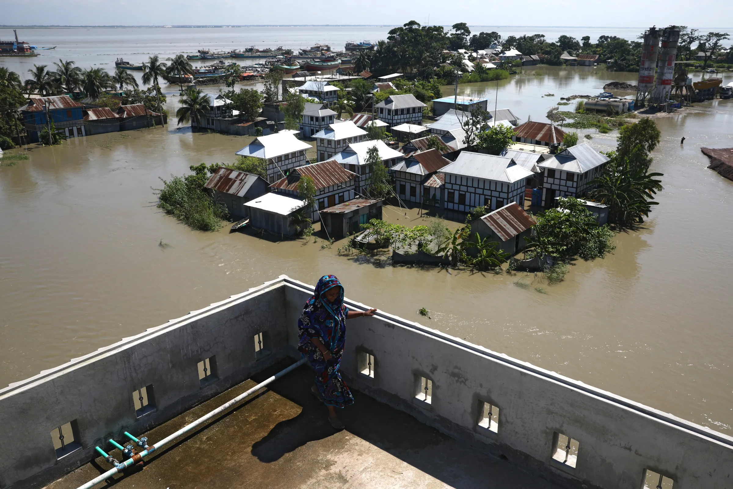 A woman looks out from a balcony at flooded houses located beside the Padma river